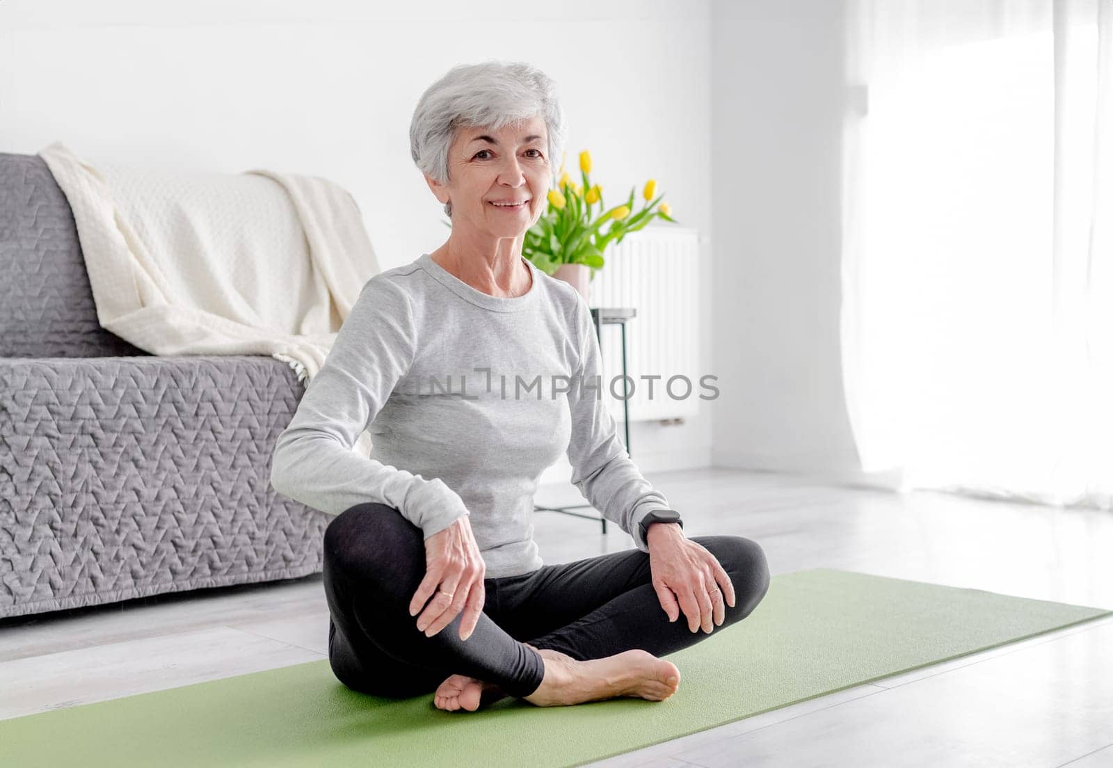 Charming Woman Looks Into Camera Sitting On Yoga Mat by tan4ikk1