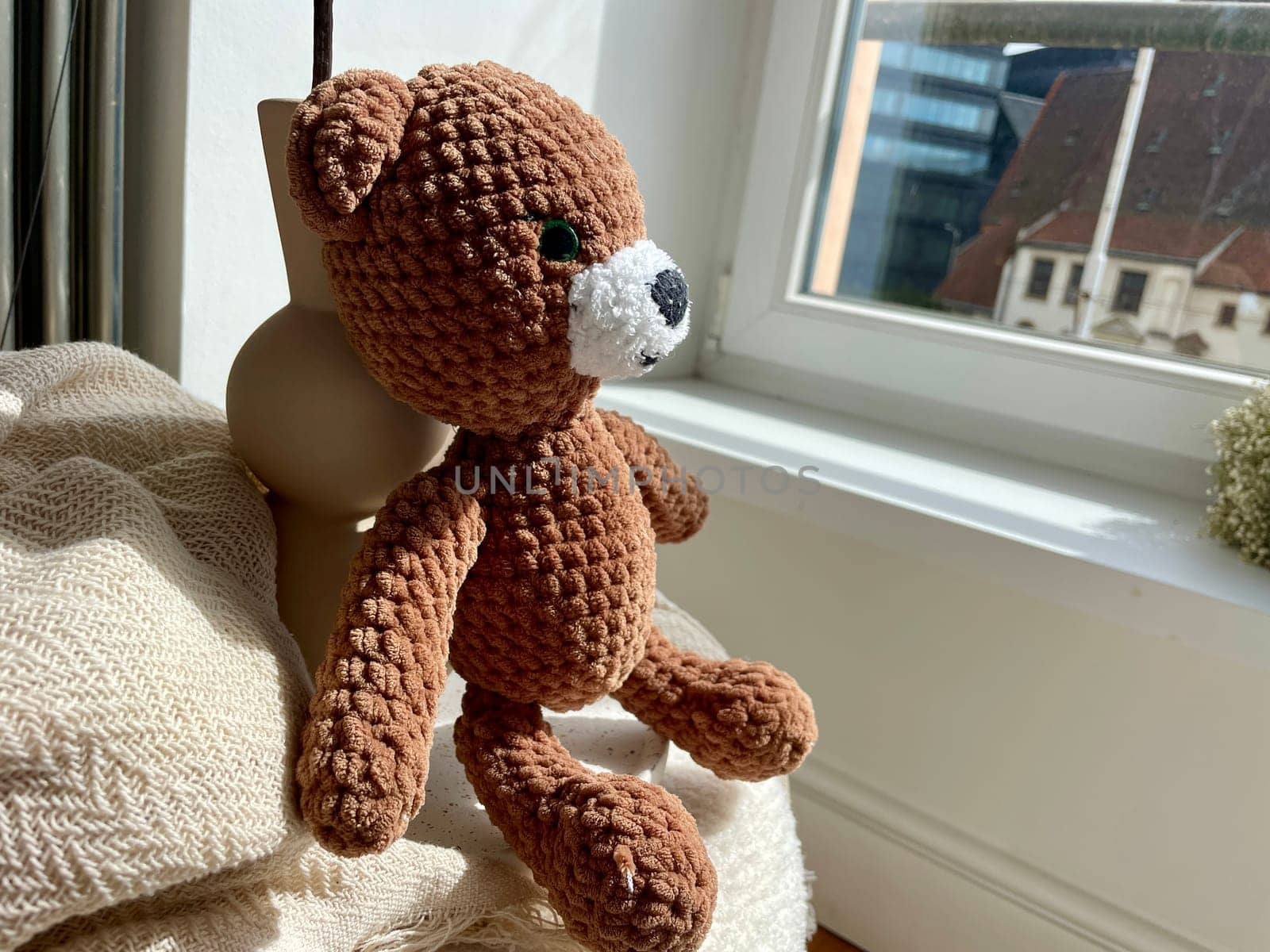 Children's toy of a knitted brown bear looking out the window. High quality photo