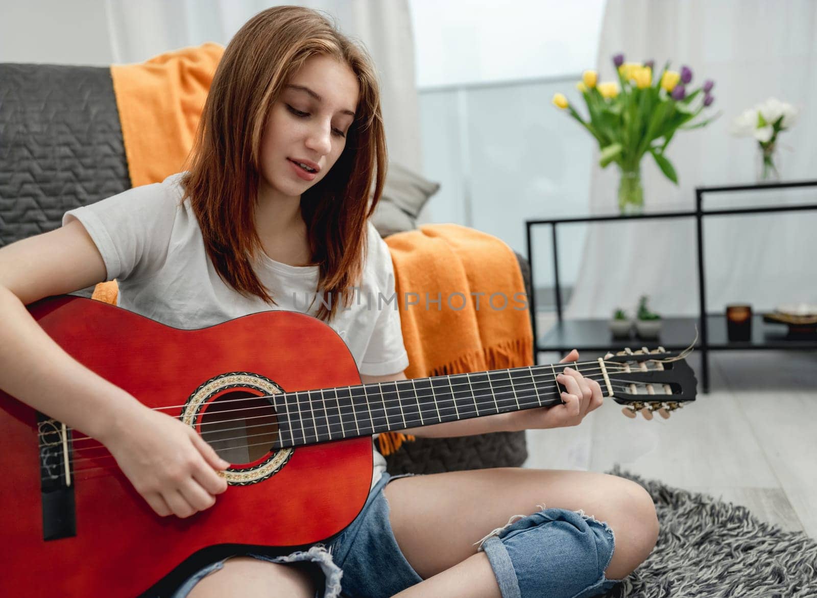 Girl teenager practicing guitar playing at home sitting on floor. Pretty guitarist with musician instrument