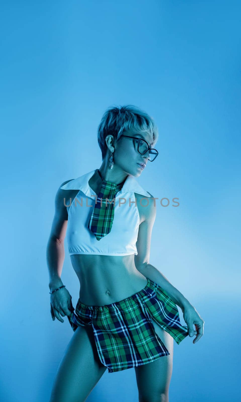 Sexy girl in an erotic school plaid skirt costume from a sex shop in blue neon light on a copy paste background