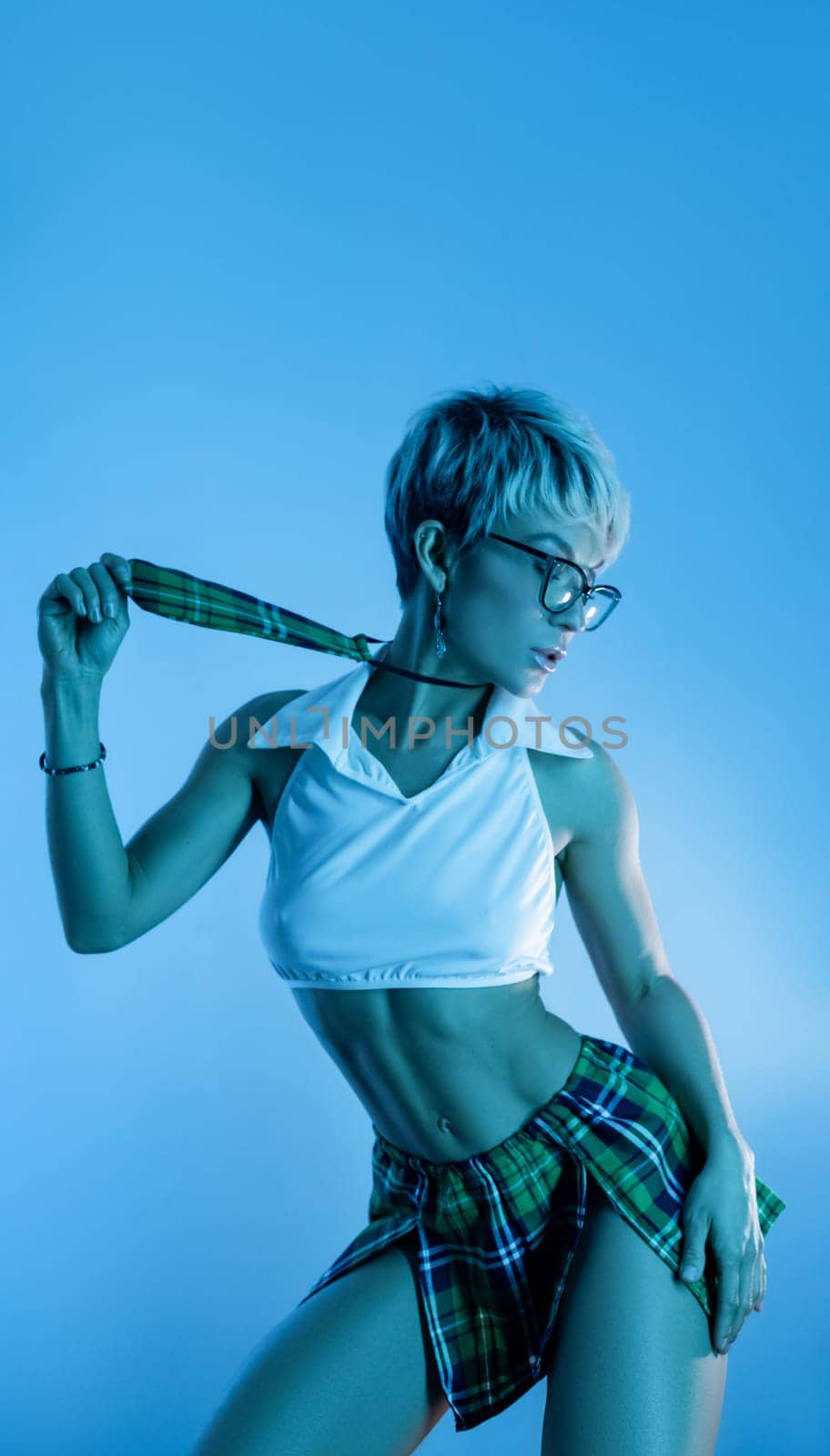 Sexy girl in an erotic school plaid skirt costume from a sex shop in blue neon light on a copy paste background