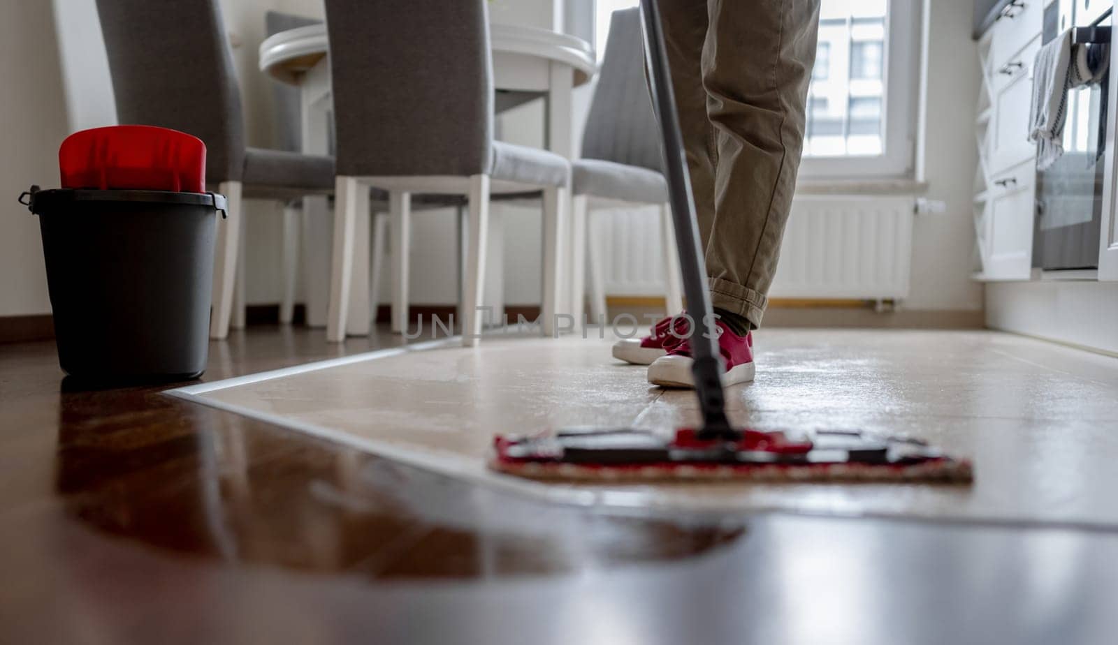 Woman Mops Floor In Kitchen With Broom Prominently In Foreground