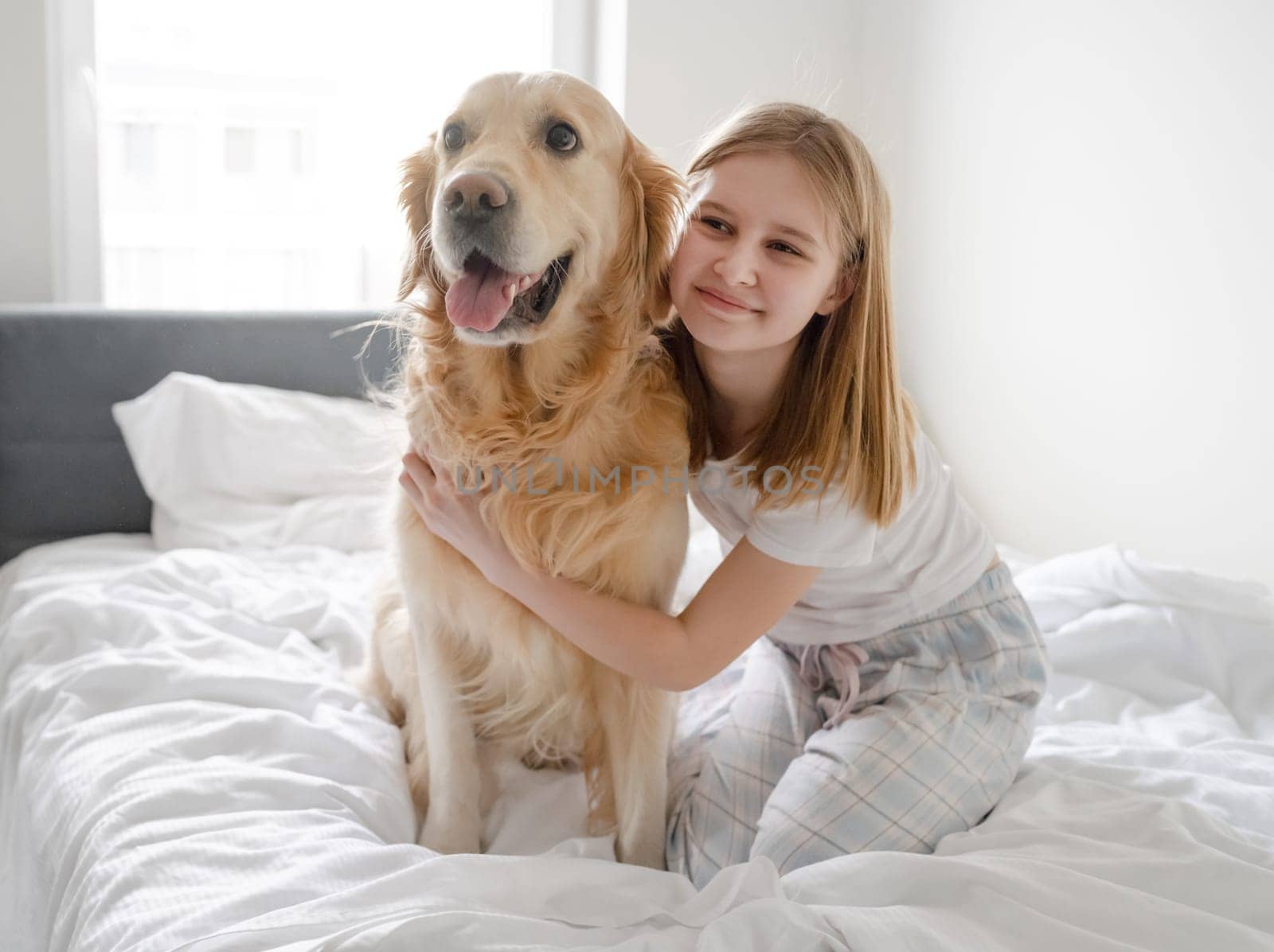 Girl Poses With Golden Retriever In Bed In The Morning In A Bright Room