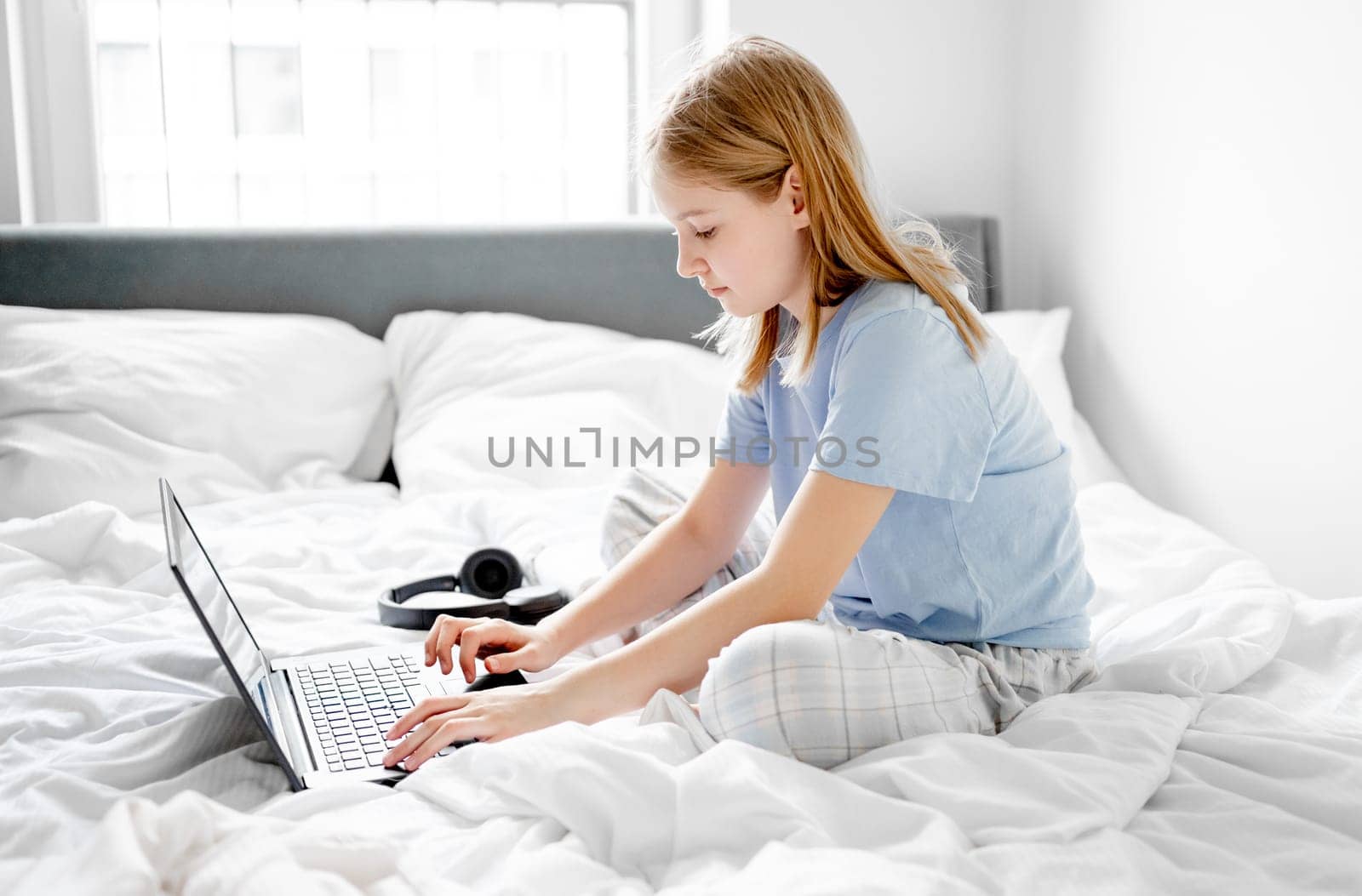 Girl Sits In Bed With Laptop In Bright Room In The Morning