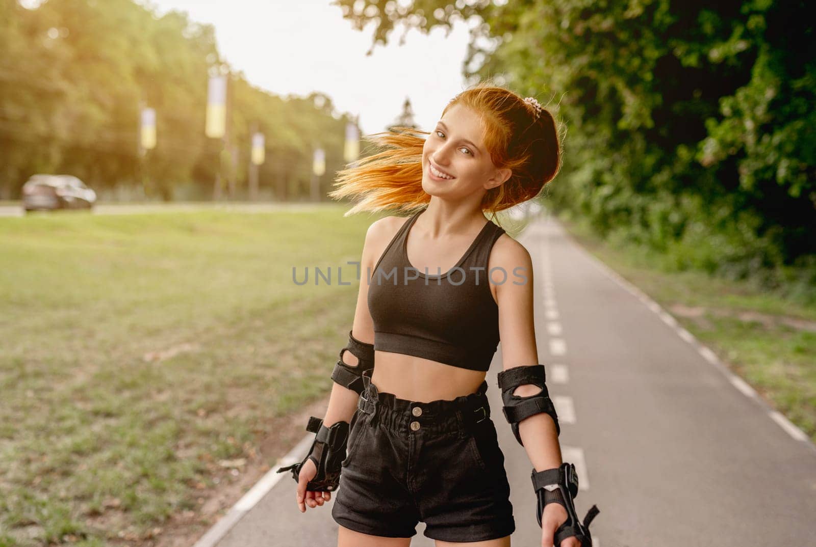 Teenage girl in sportswear enjoying roller skating in summer park