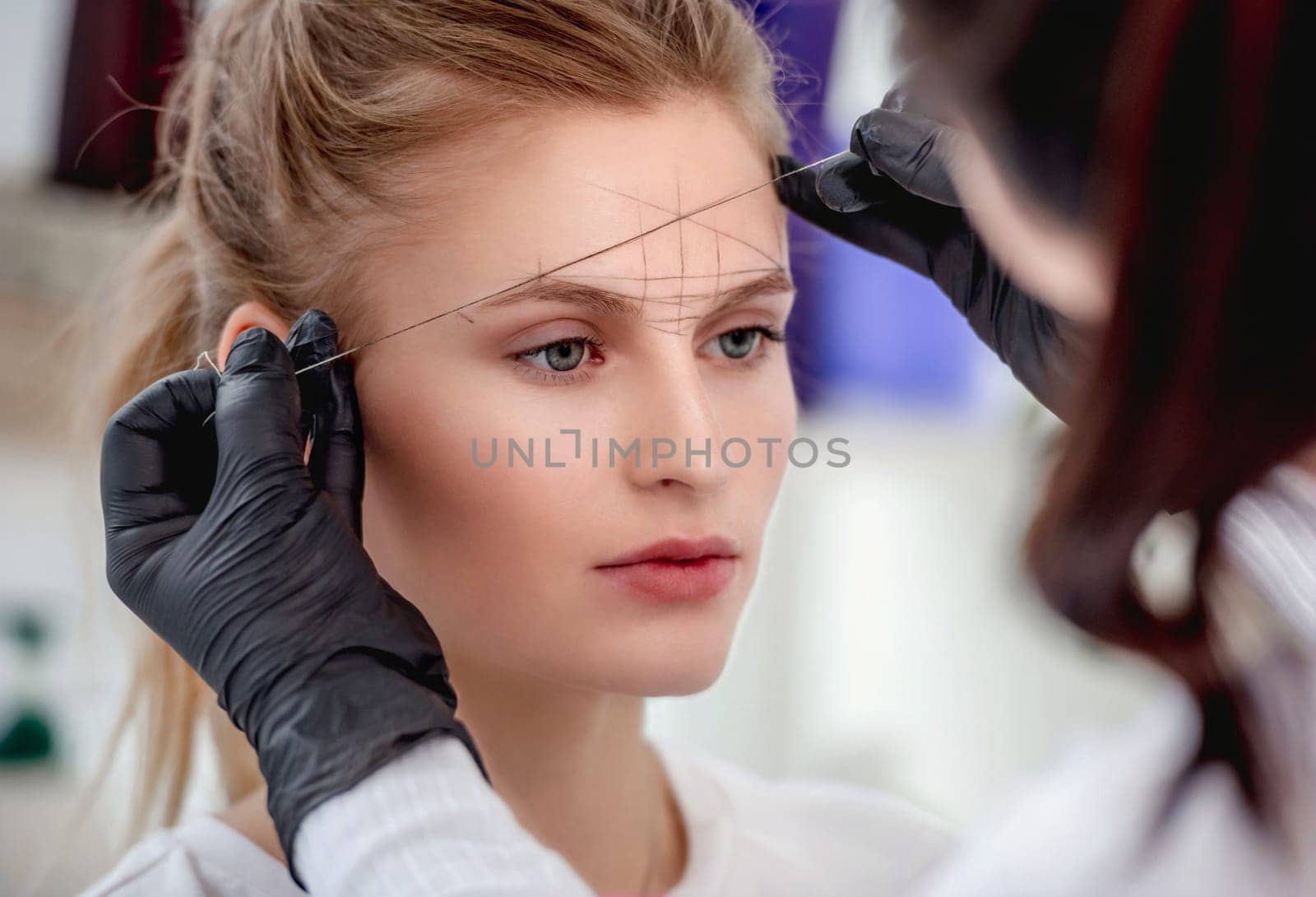 Permanent tattoo makeup master defines the ideal eyebrow shape with professional tools. Closeup view of microblading work process