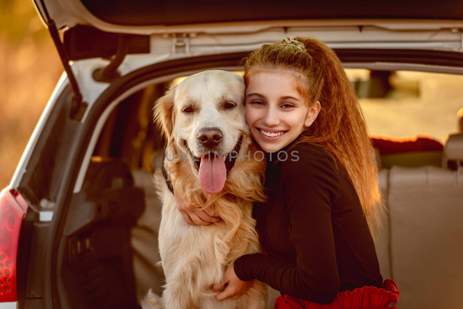 Teenage girl hugging dog in car trunk by tan4ikk1
