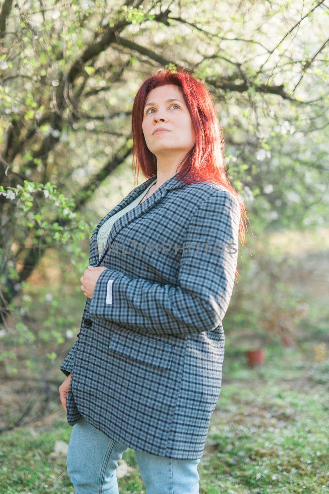 Beautiful young red hair woman near blooming spring trees alley. Youth and love, fashion and romantic and lifestyle concept