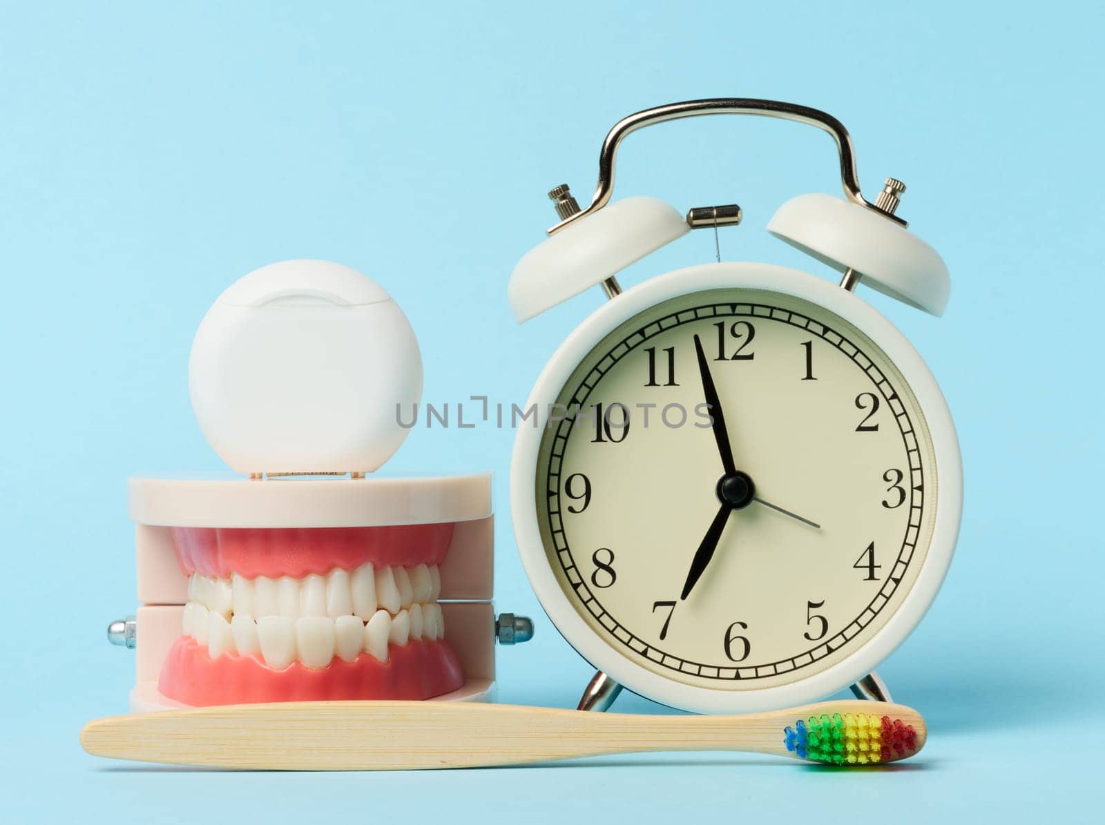 Plastic model of human jaw, alarm clock and dental floss on blue background by ndanko