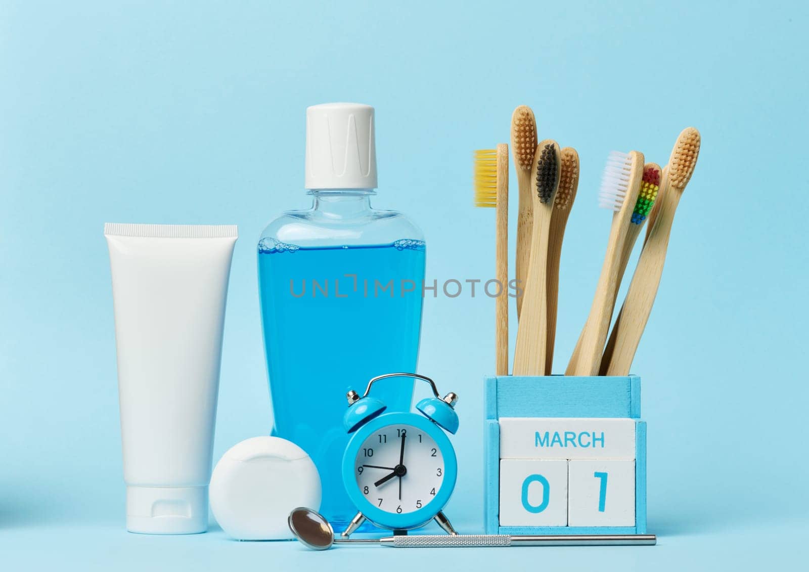 Mouthwash and toothpaste tube, alarm clock on blue background