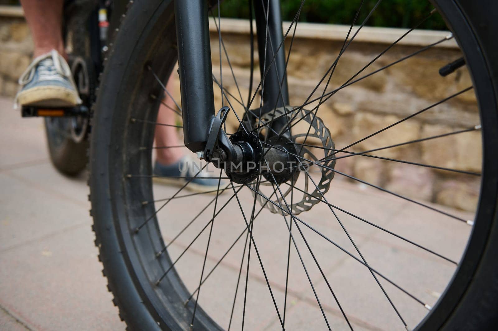 Details on electric bike bicycle wheel with spokes. Cropped view of a man cycling in the nature. Cyclist renting electric bike as comfortable, ecologically friendly public transport. Closeup by artgf
