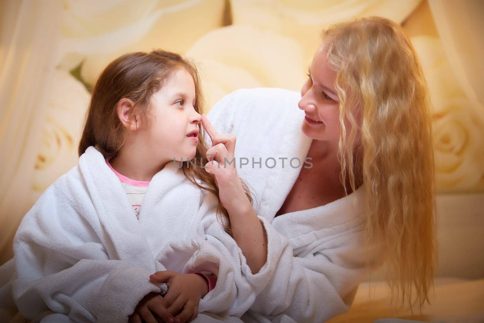 Mother and daughter happily relax and fun together on bed in bedroom. The concept of tenderness between mom and girl