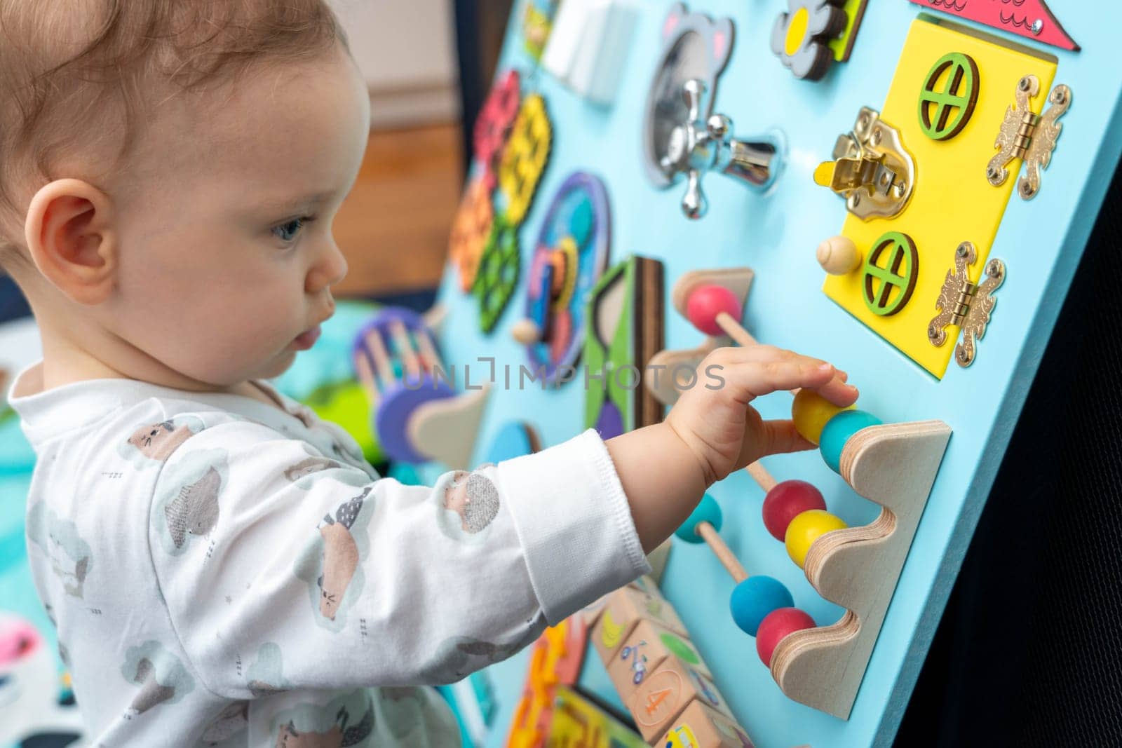 A baby moves wooden elements on a busy board.