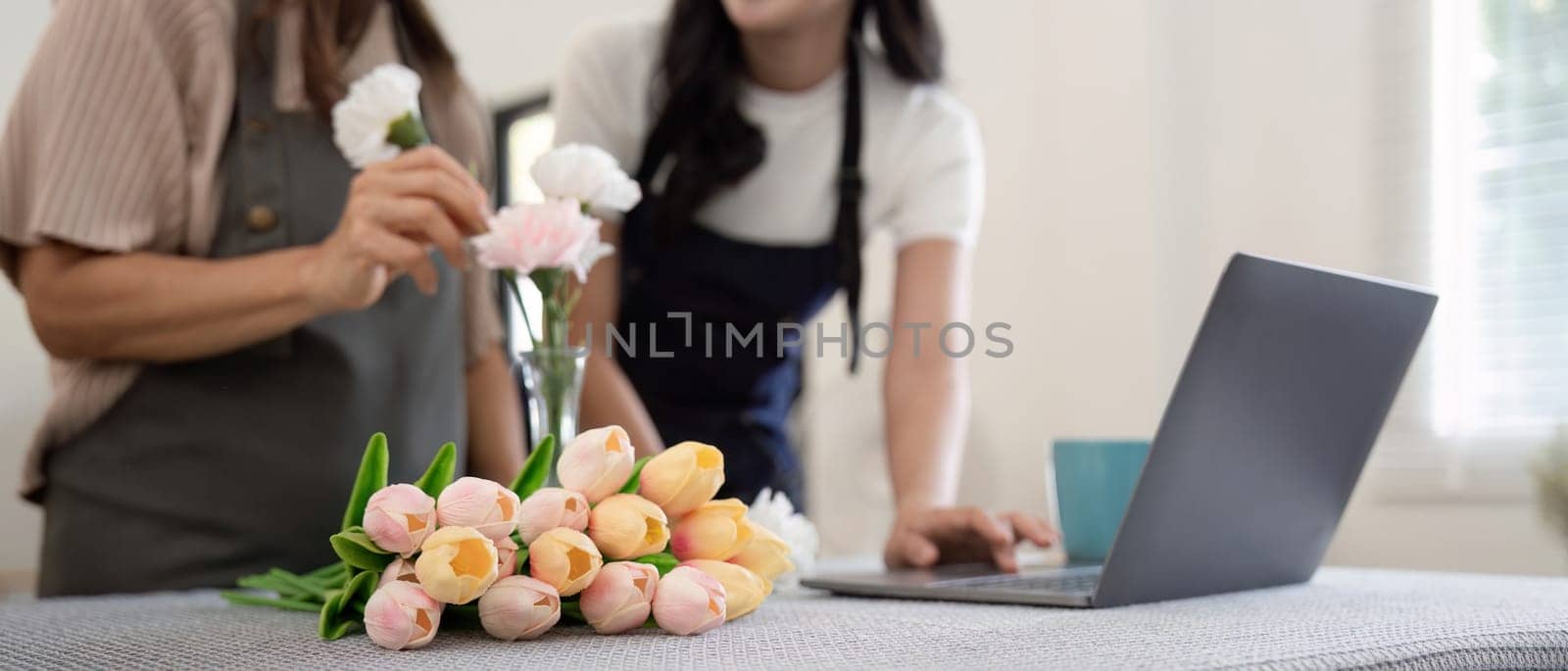 Senior mother and adult daughter happy on the table while arrange flowers in a vase together using laptop computer. lifestyle concept. Happy time together by nateemee