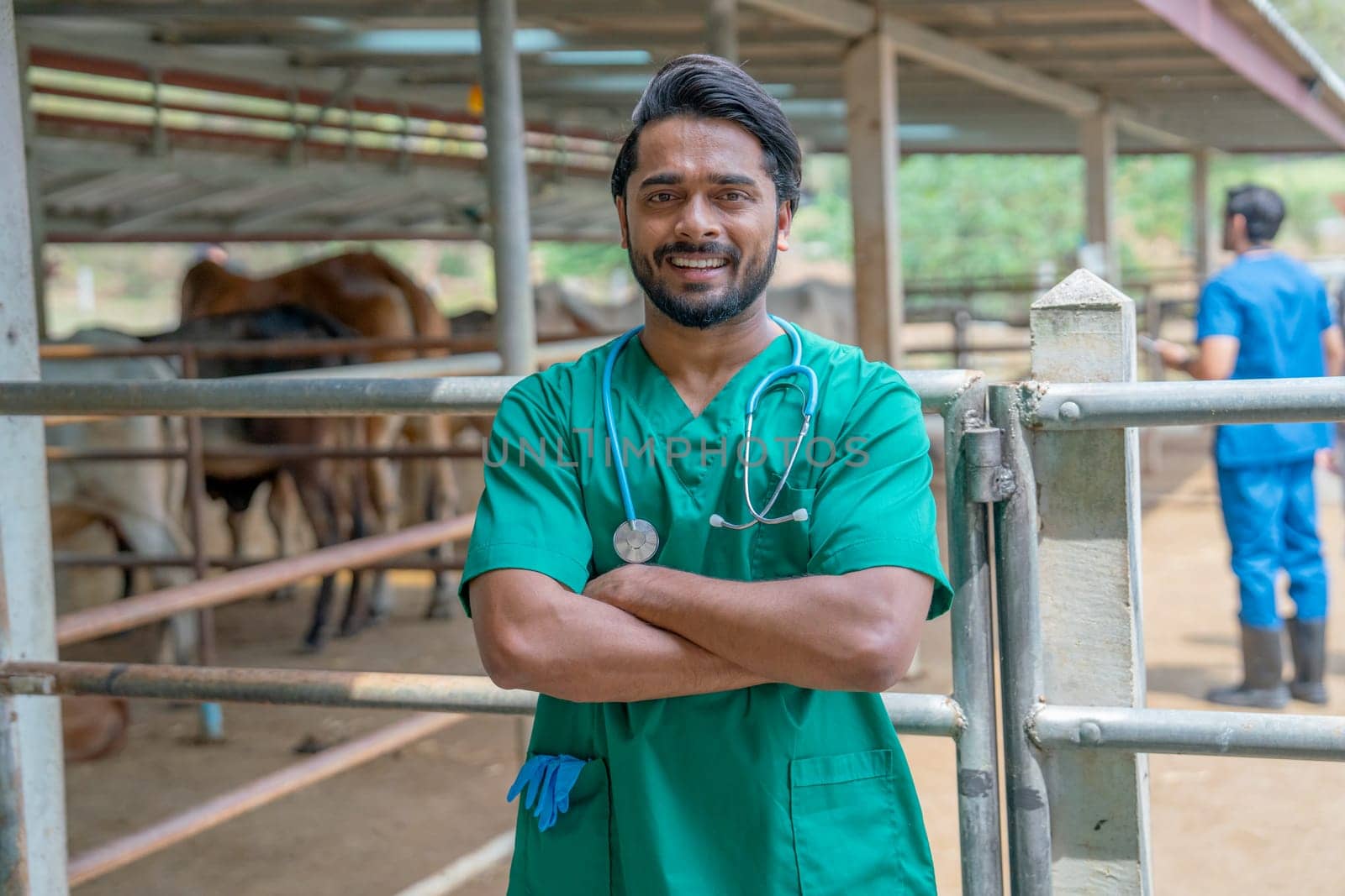 Portrait of Asian veterinarian stand with arm-crossed in front of cow stable also look at camera with smiling and his team also work in the background. by nrradmin