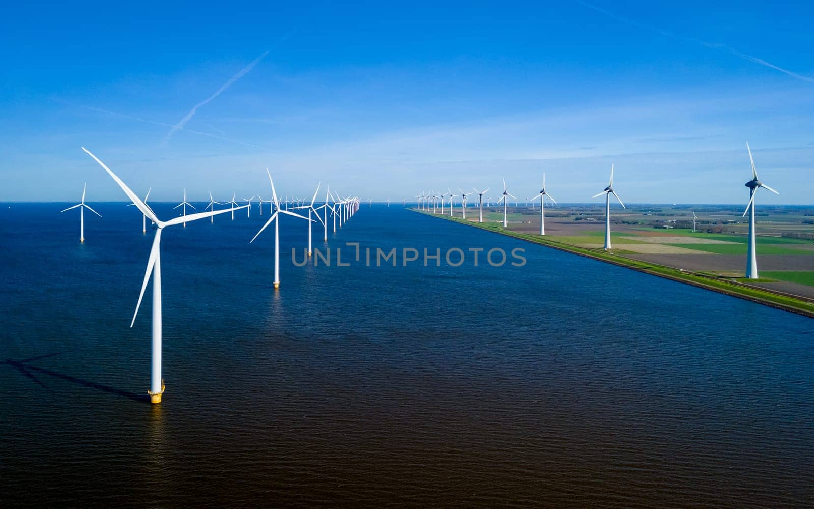 An expansive body of water in the Netherlands Flevoland is dotted with numerous towering windmills, by fokkebok