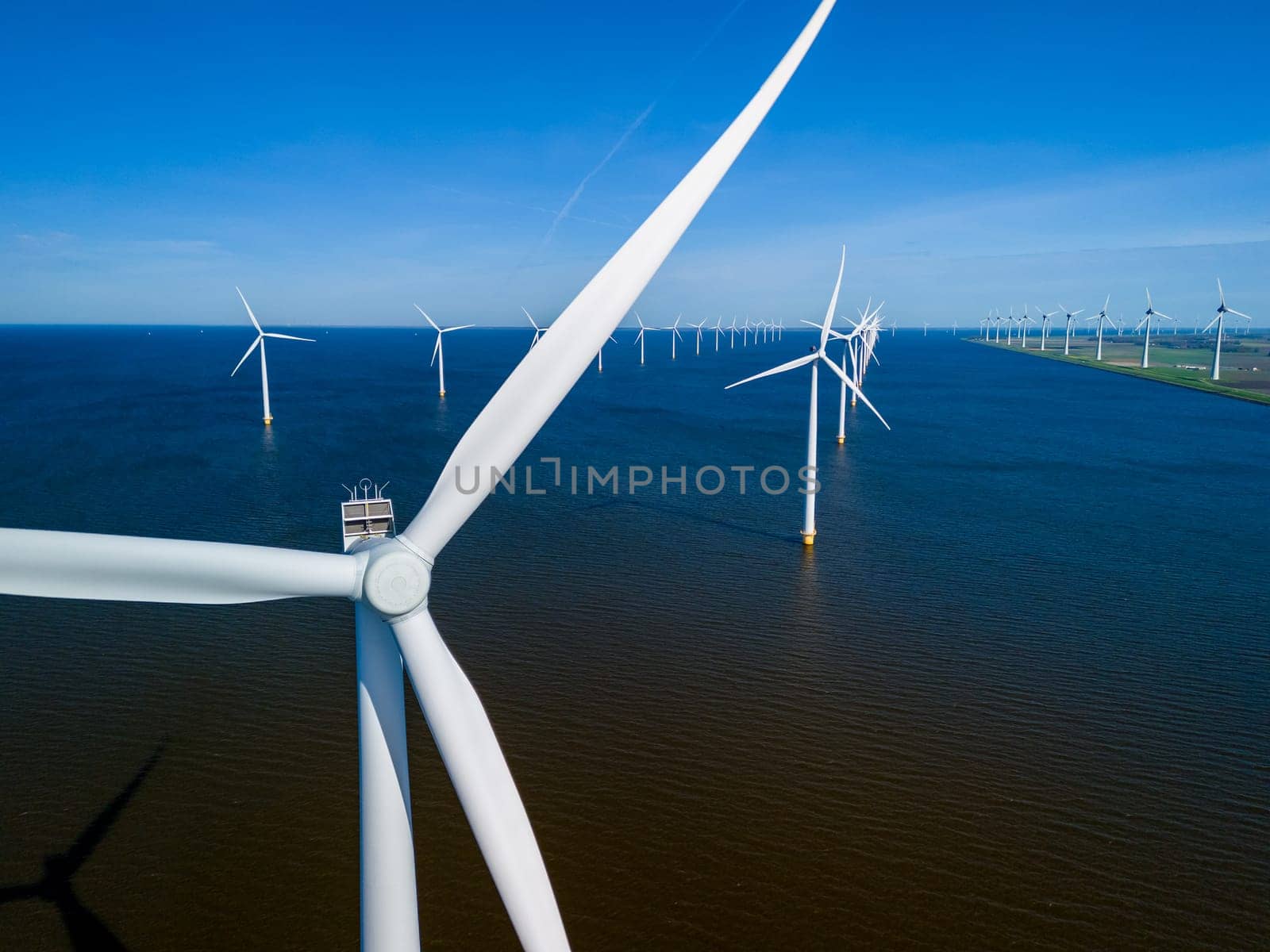 A group of picturesque windmills from the Netherlands Flevoland region gracefully float atop a tranquil body of water on a beautiful Spring day. windmill turbines green energy in the ocean