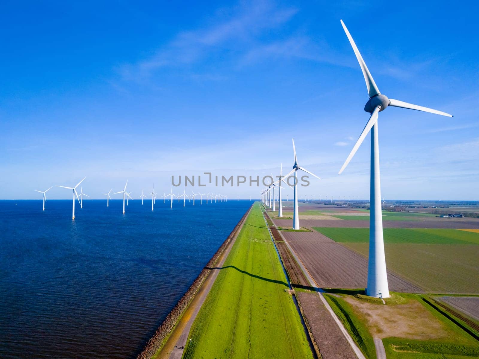 A row of elegant wind turbines stand tall by a vast body of water in the Netherlands Flevoland, reflecting the harmony between nature and renewable energy.