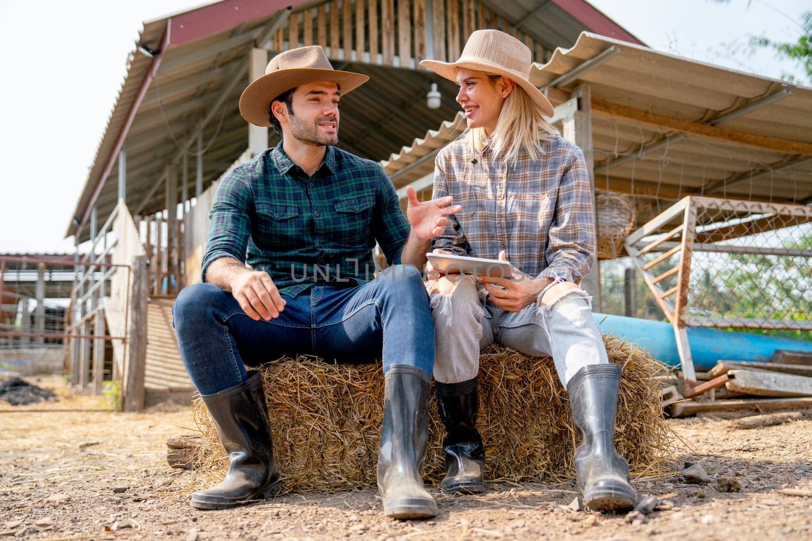 Caucasian man and woman farmers sit on straw and discuss about working with man explain the process and they look happy and relax after work in farm together with day light.