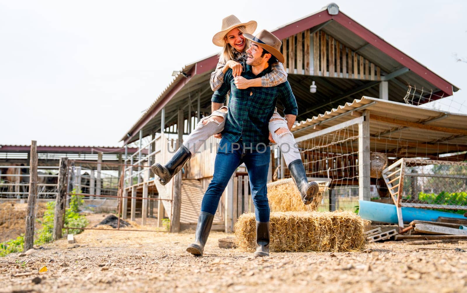 Wide shot of Caucasian man and woman farmer enjoy with woman riding on the back of man and go around the area of their farm with happiness and day light. by nrradmin