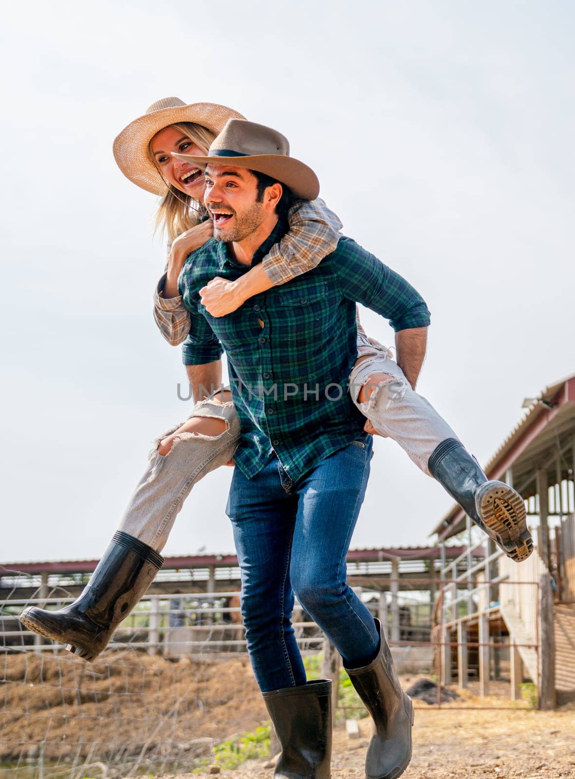 Vertical image of Caucasian man and woman farmer enjoy with woman riding on the back of man and go around the area of their farm with happiness and day light. by nrradmin