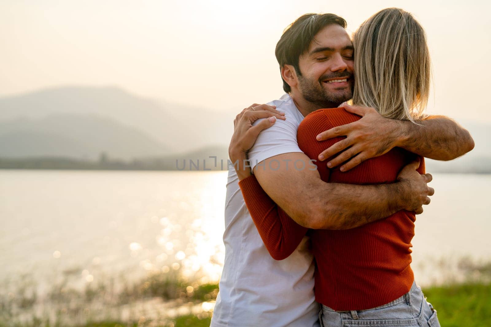 Close up Caucasian man hug with his lover woman near lake with romace and sunset light and they look happy and enjoy together. by nrradmin