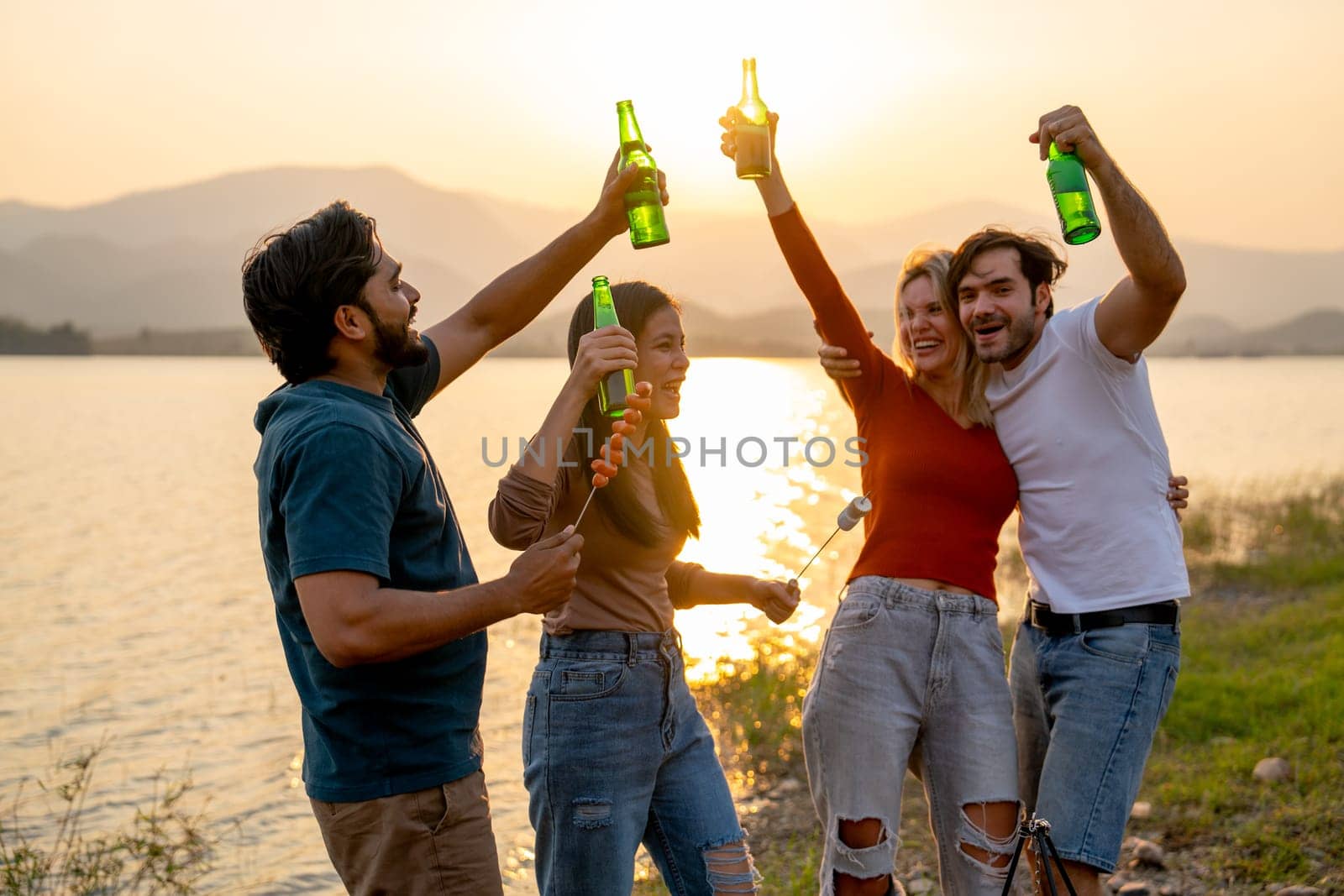 Group of friends with multi-ethnic enjoy with dancing and hold bottle of drinking in public park near the lake with sunset light. by nrradmin