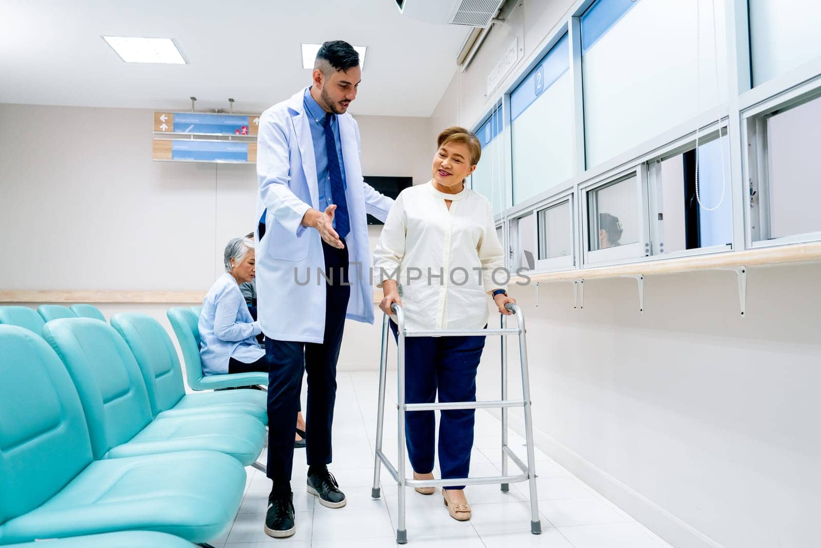 Portrait of Caucasian doctor help to take care and support senior patient woman with walker to walk in front of pharmacy counter in hospital.
