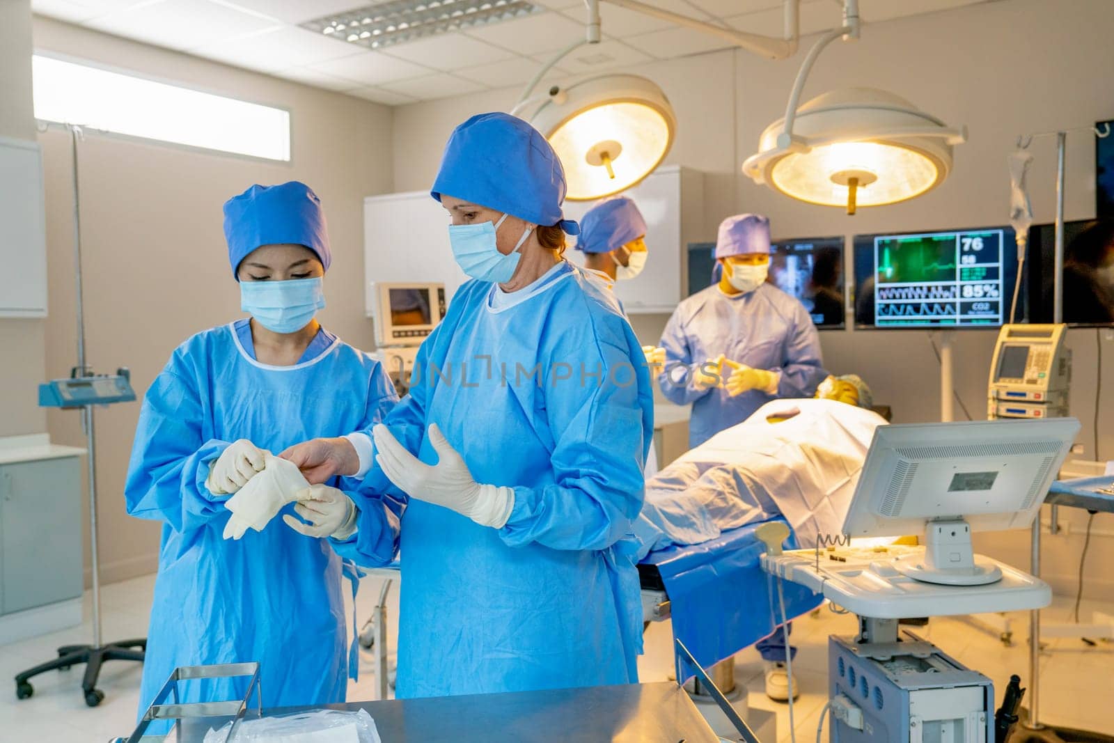 Professional nurse help the doctor to wear surgical gloves before process of operation in the room with their team in the back.
