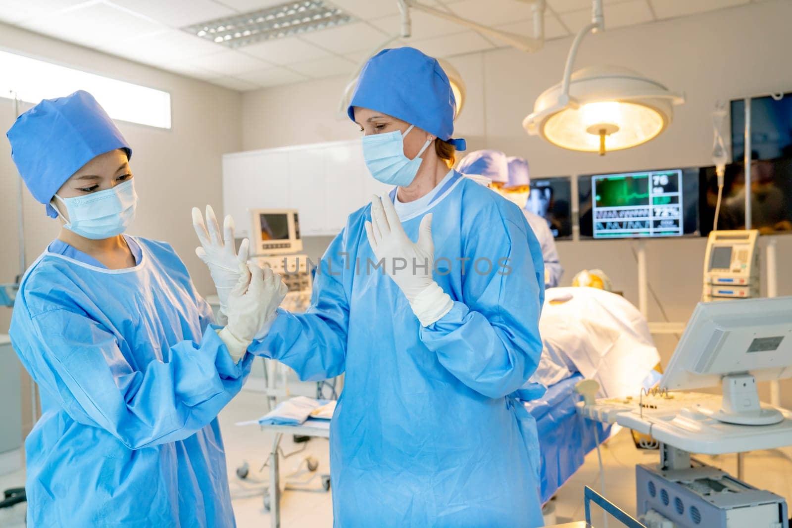 Portrait of nurse help the doctor to wear surgical gloves before process of operation in the room with their team in the back. by nrradmin