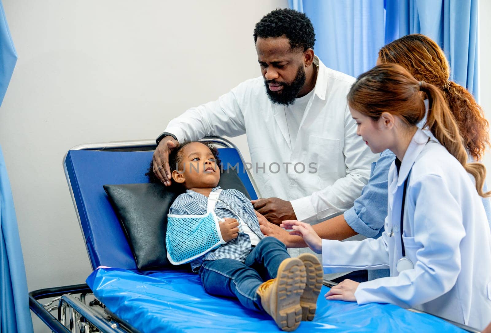 African American father take care little daughter lie on bed with arm injury and also take care by woman doctor.