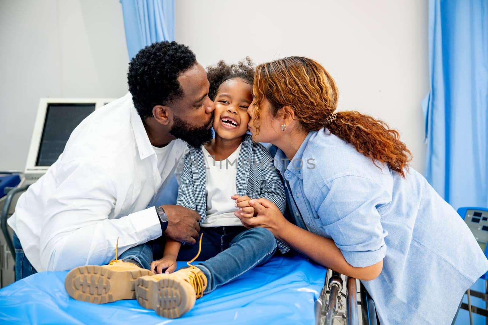 African American father kiss little girl with Asian woman as his wife and little look happy and sit on patient bed in the hospital.
