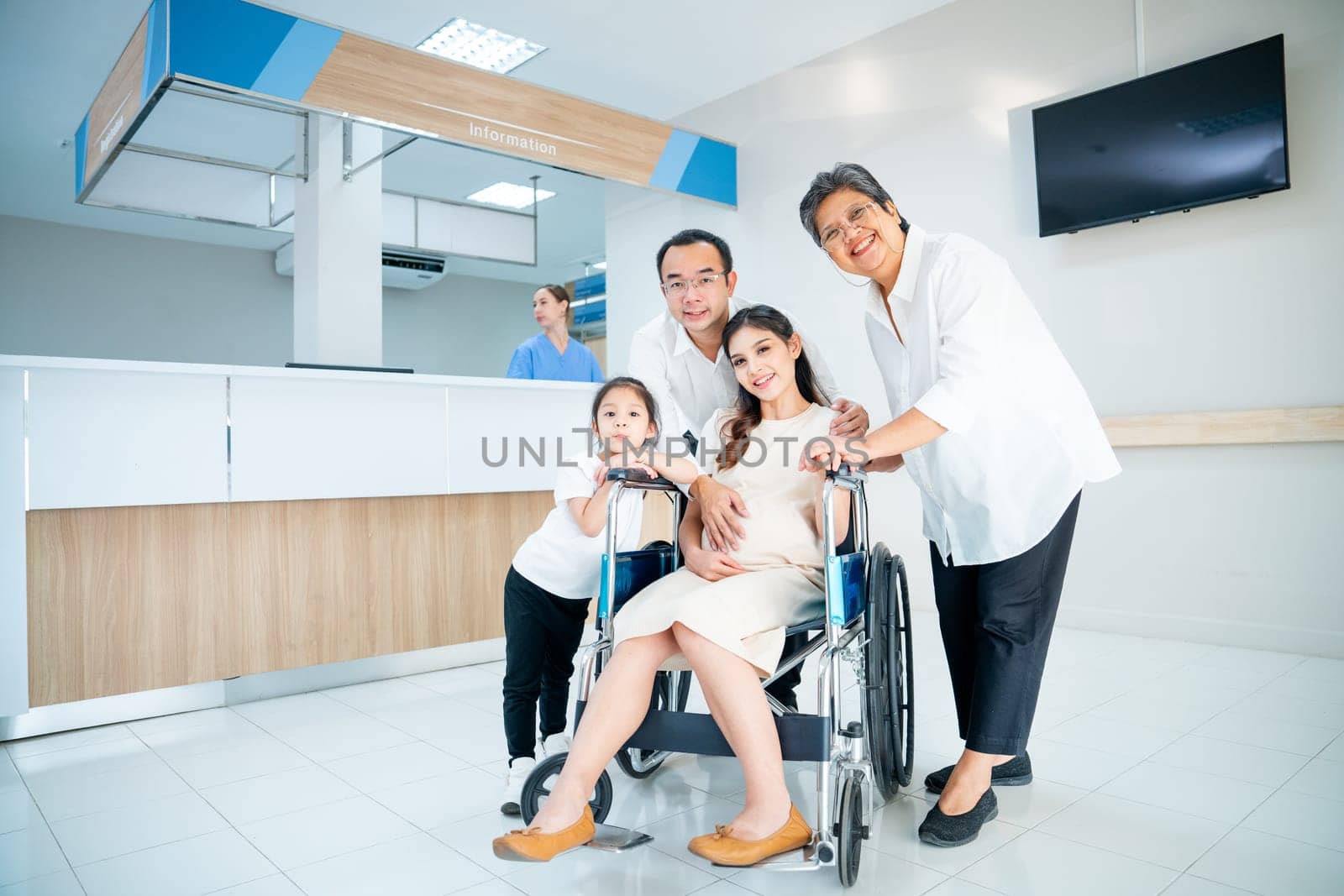 Asian family with grandmother, pregnancy woman, man and daughter stay in front of registration counter in hospital and they look at camera with happiness. by nrradmin
