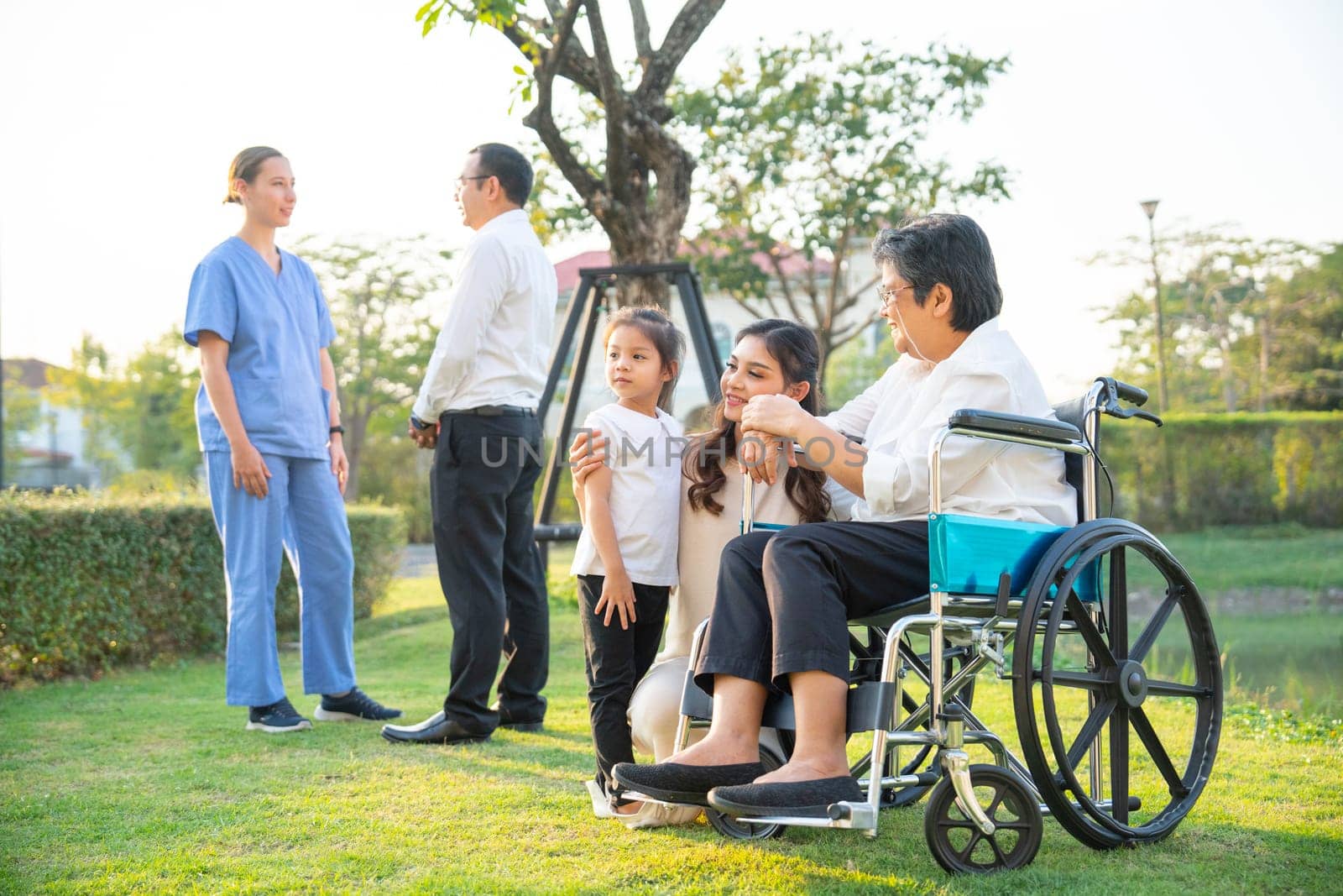 Asian family stay in garden in area of their home village with soft light in evening and look happy with man discuss with doctor in the background. by nrradmin