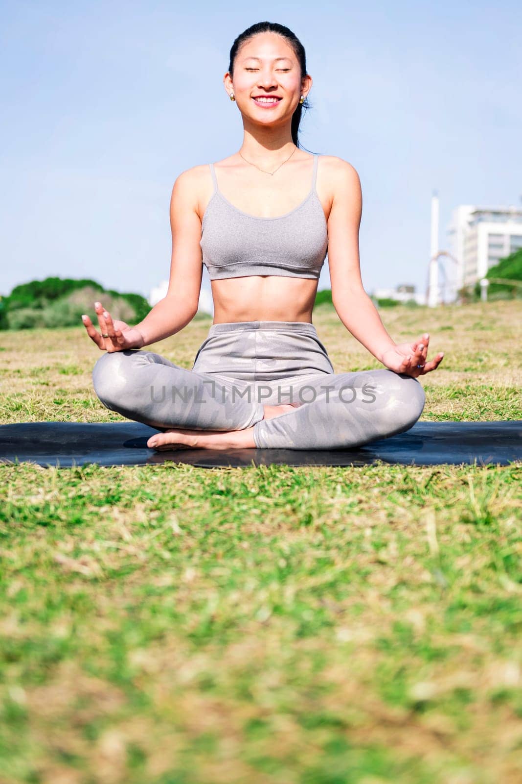smiling young asian woman doing meditation at park sitting on a yoga mat, concept of mental relaxation and healthy lifestyle, copy space for text