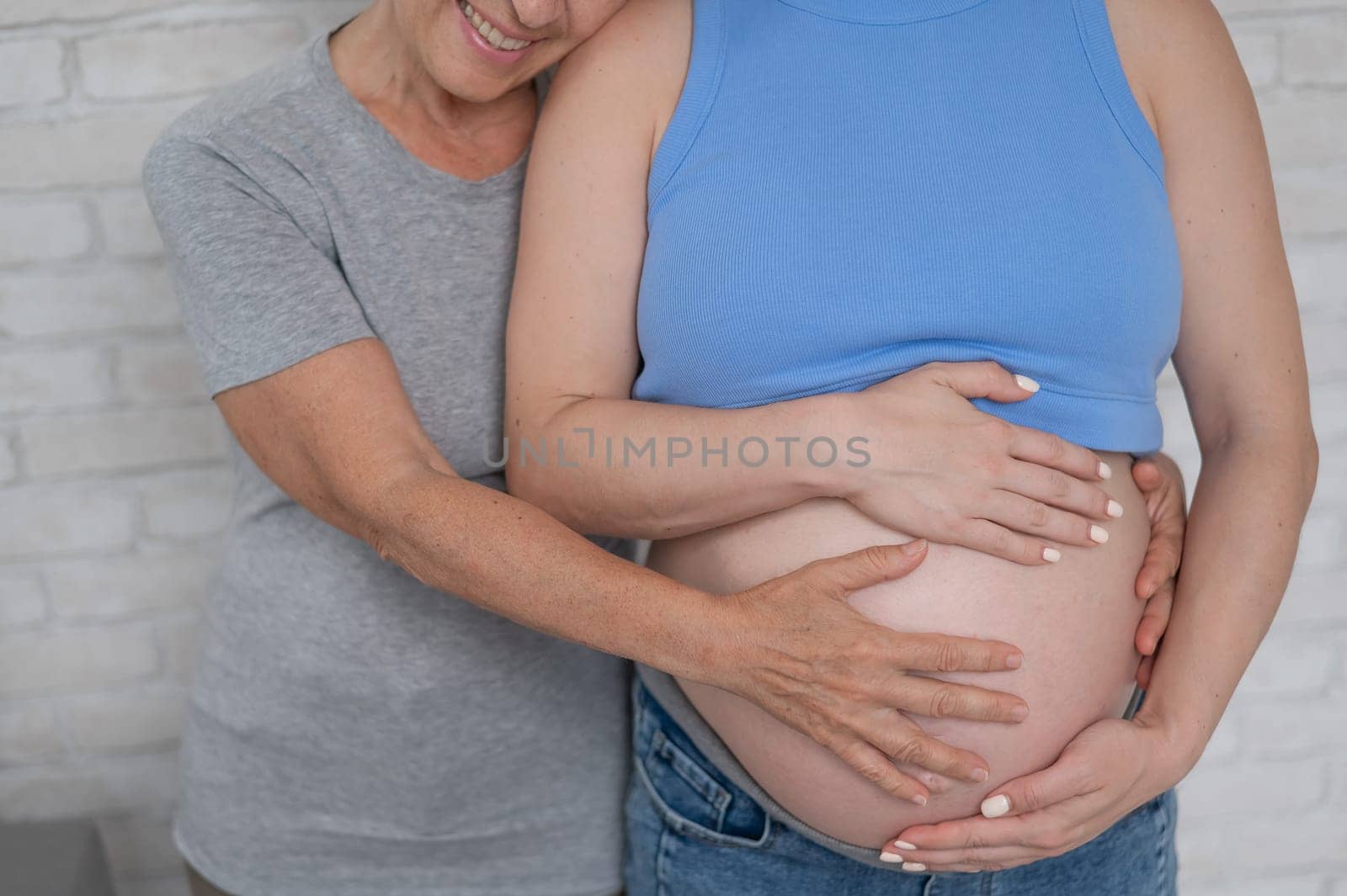 An elderly woman touches the belly of her pregnant daughter. Close-up. by mrwed54