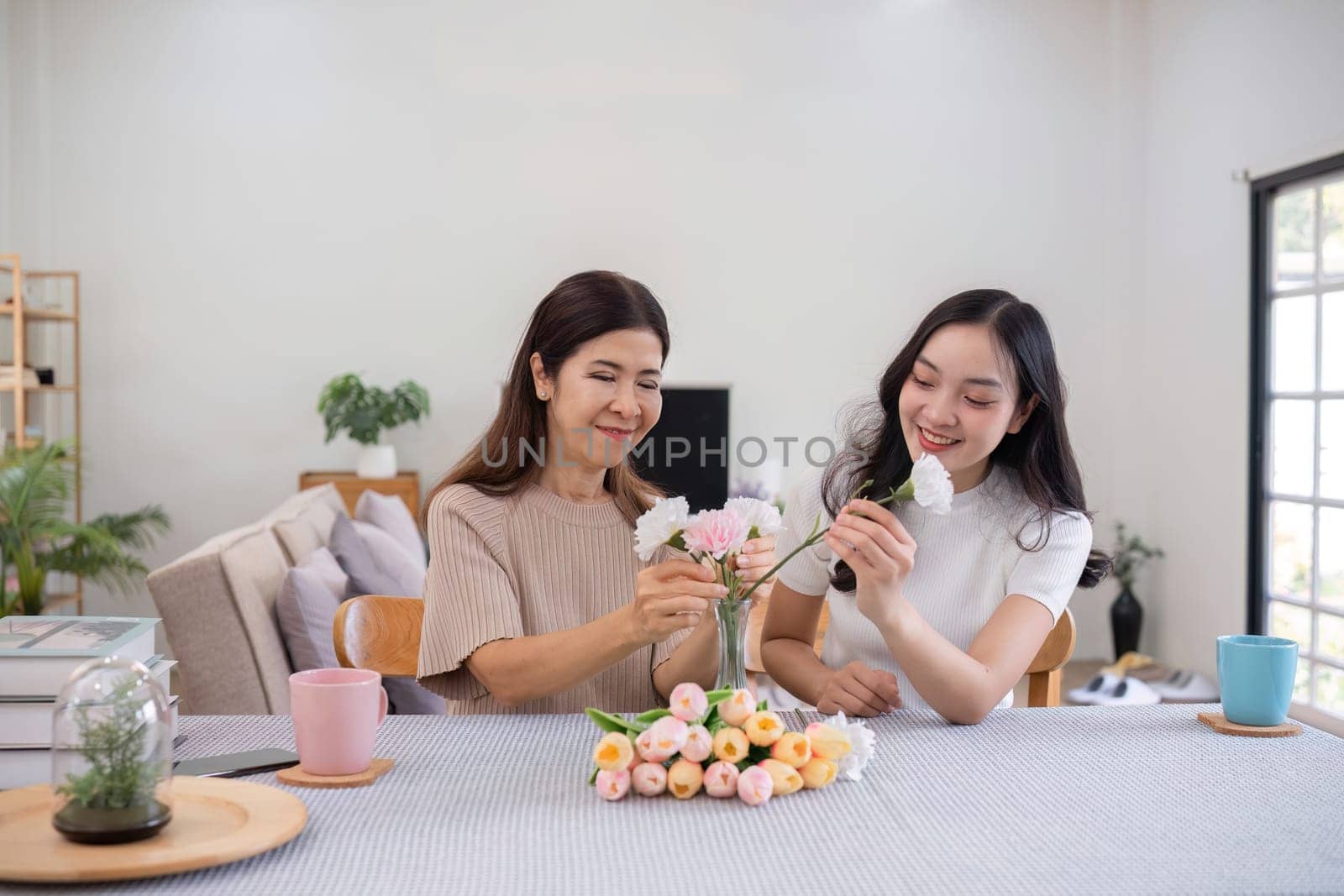 Middle-aged daughter happily arranges flowers with her mother at home Free time activities that are done together as a family by wichayada