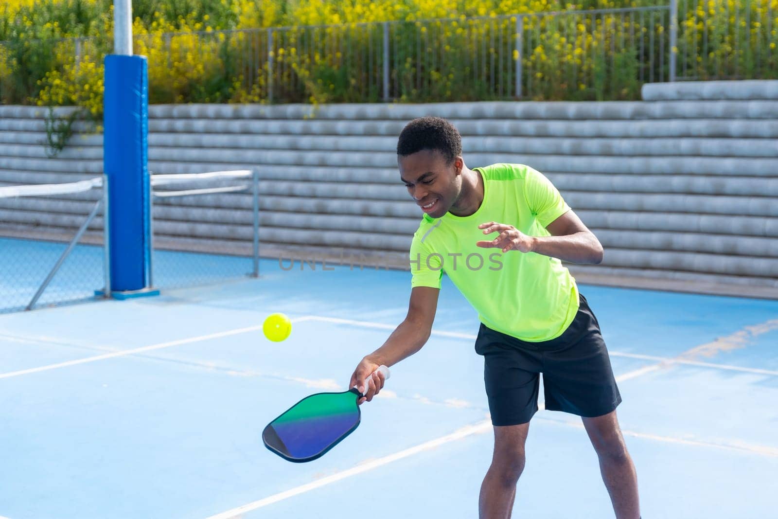 African young man playing pickleball in an outdoor court by Huizi