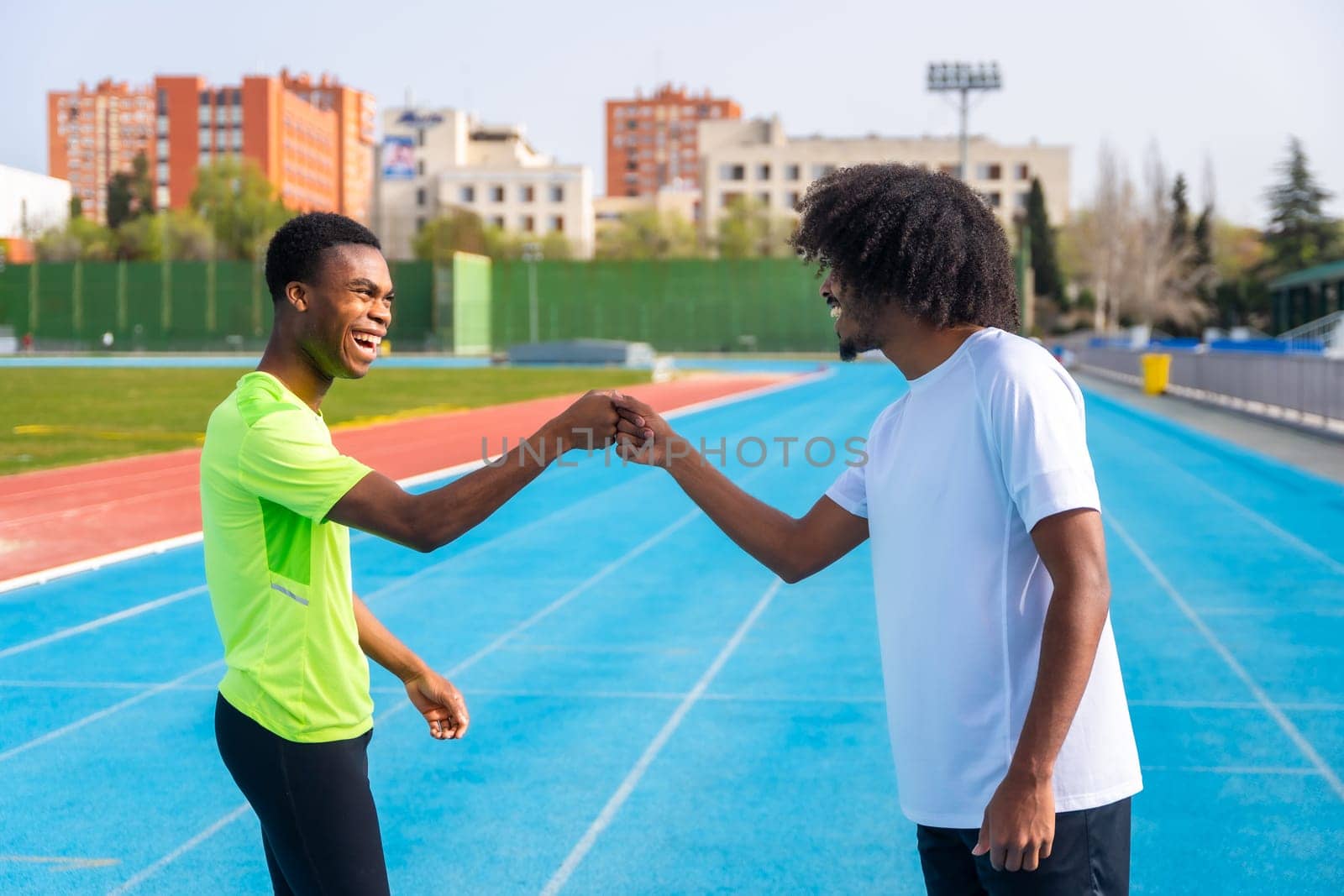 Runners fist bumping before training on an outdoor track by Huizi