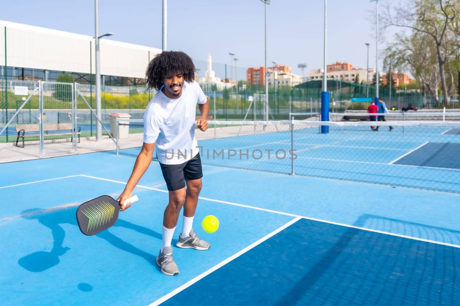 Smiling man with afro hair serving while playing pickleball by Huizi