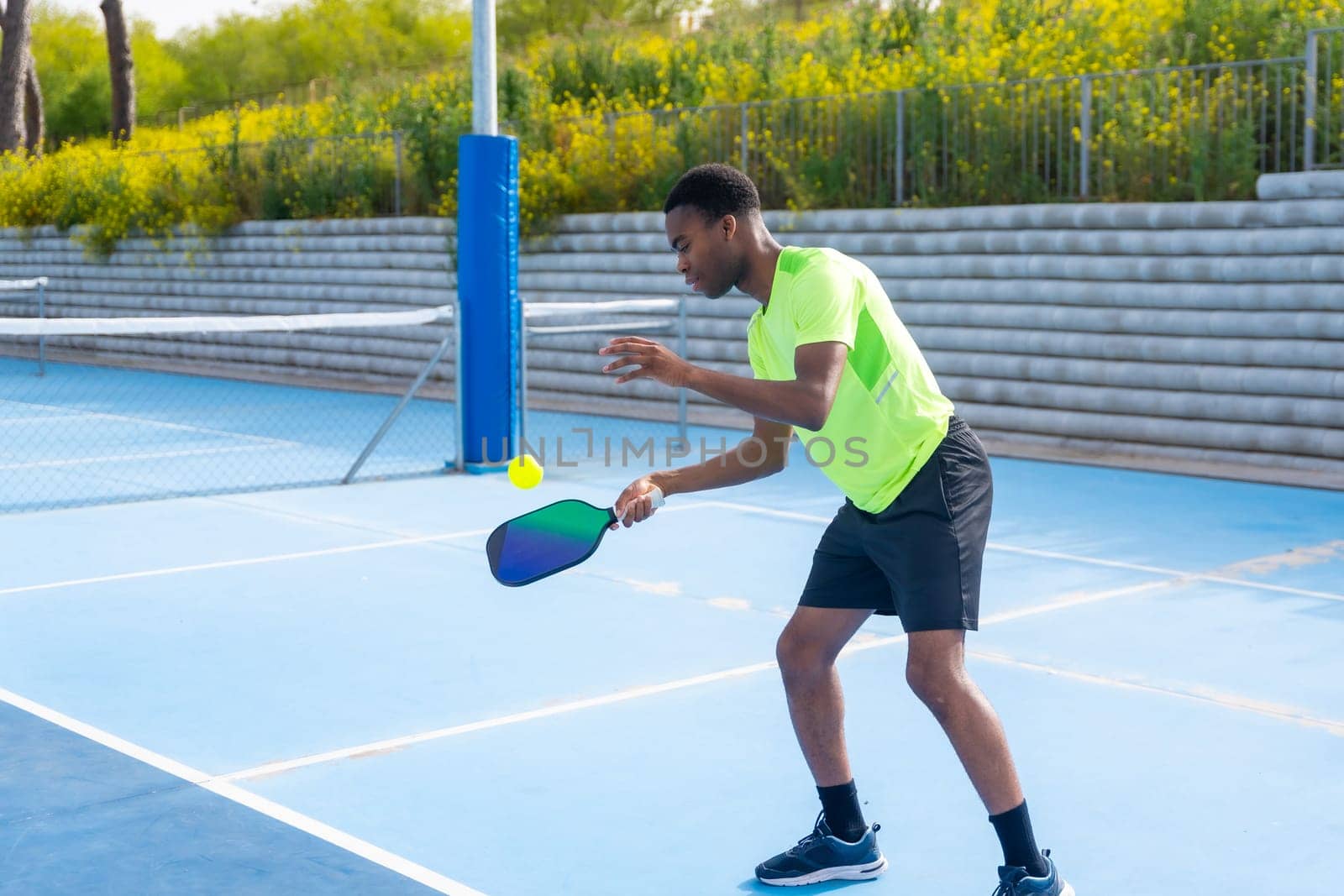 Side view photo with copy space and full length of an african american young man using racket to play pickleball outdoors