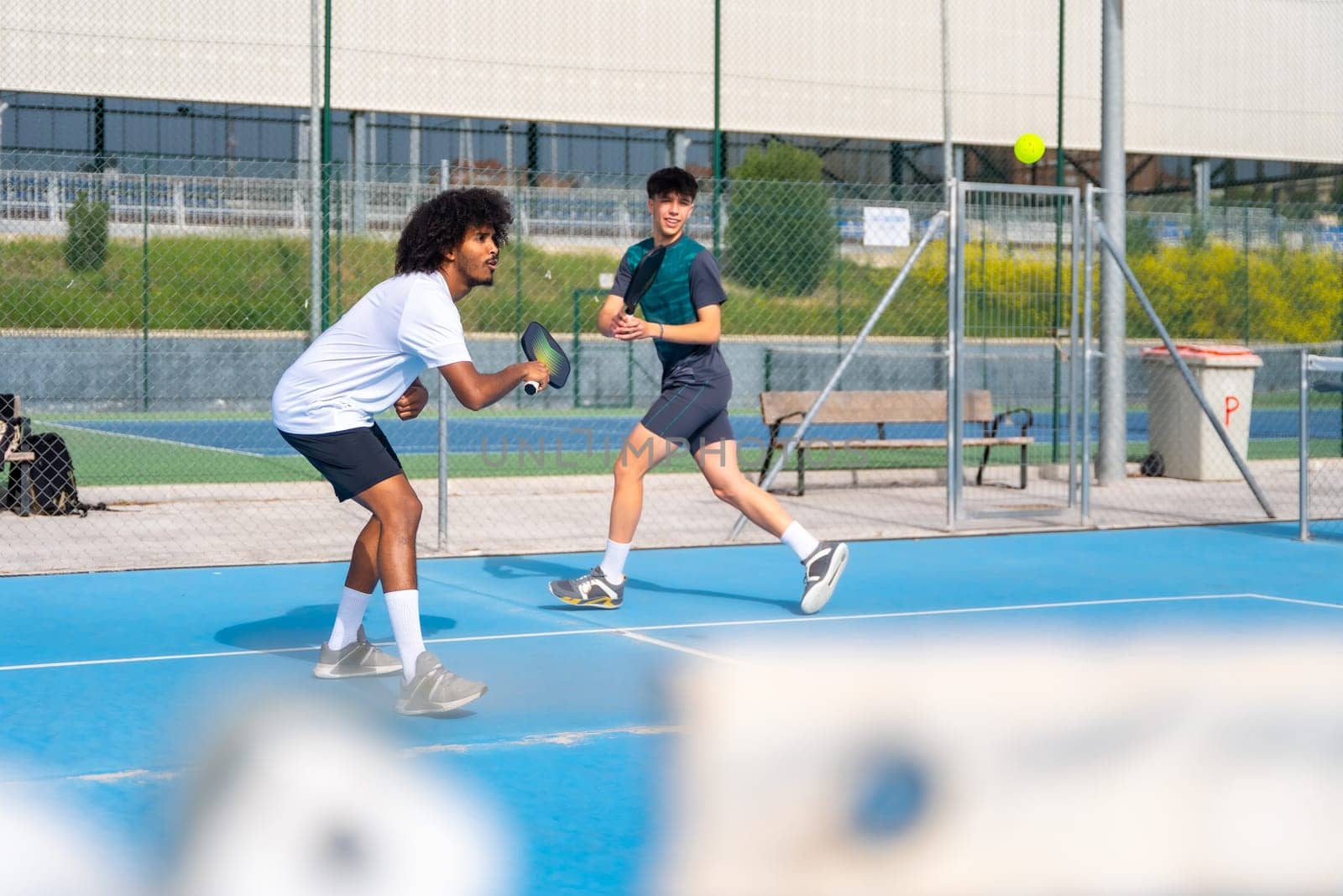 Multi-ethnic young sportive friends playing pickleball outdoors by Huizi