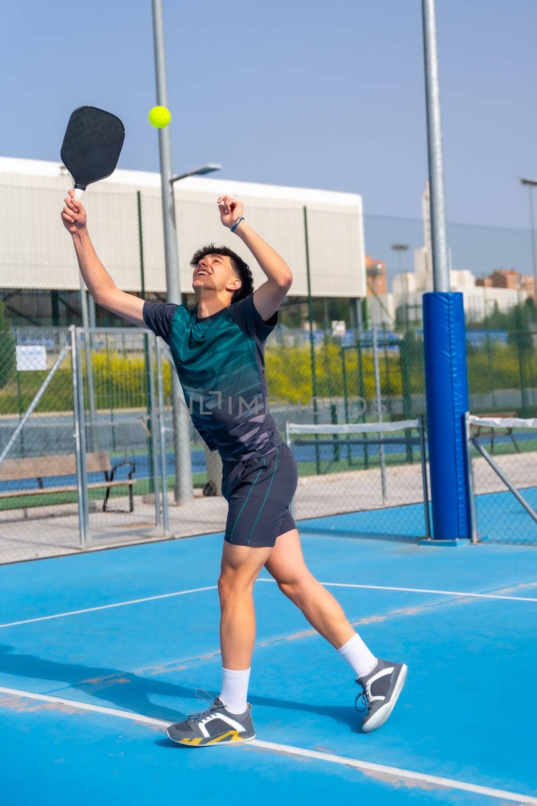 Vertical full length photo of a caucasian young sportive man trying to reach the ball playing pickleball outdoors