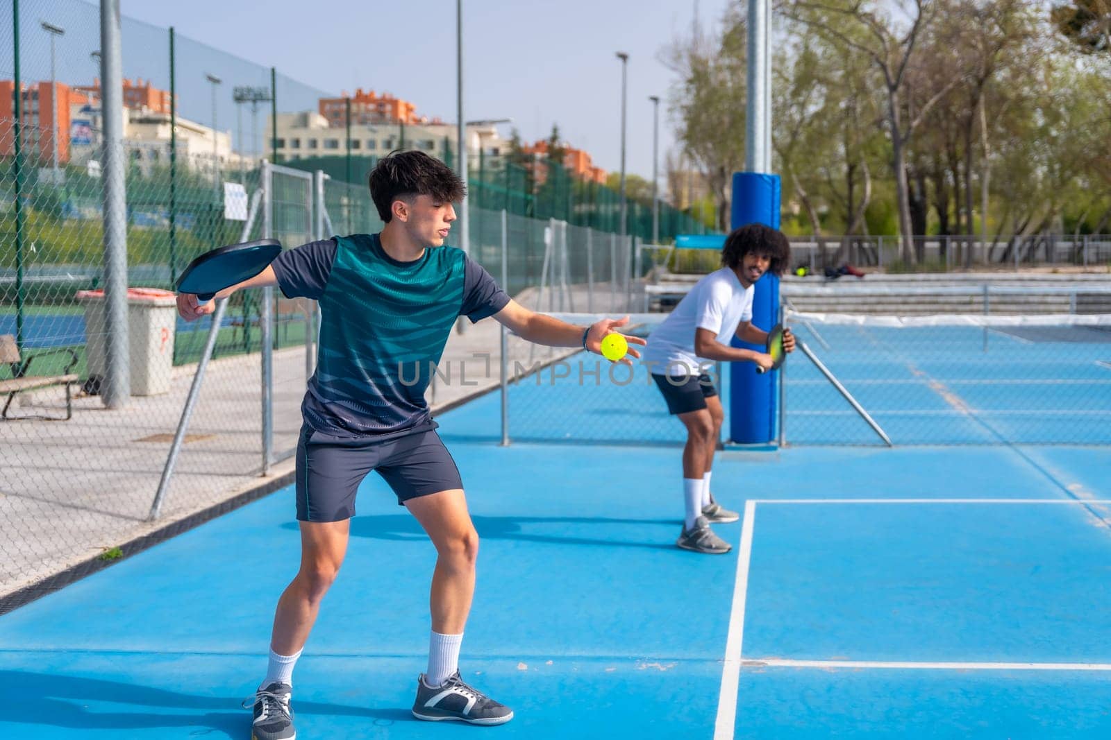 Man serving ball playing pickleball with partner by Huizi