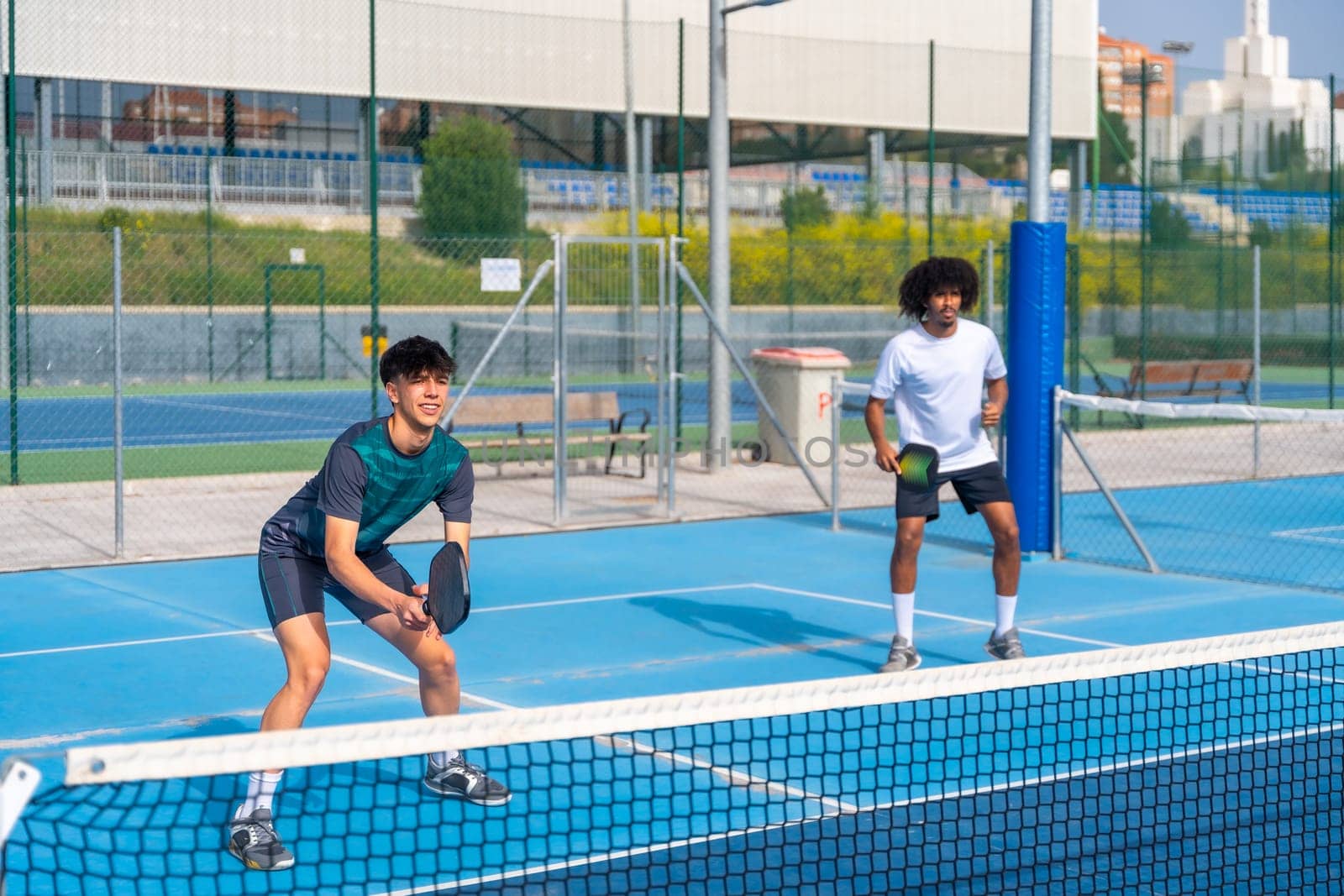 Multiracial pickleball team partners playing in an outdoor court by Huizi
