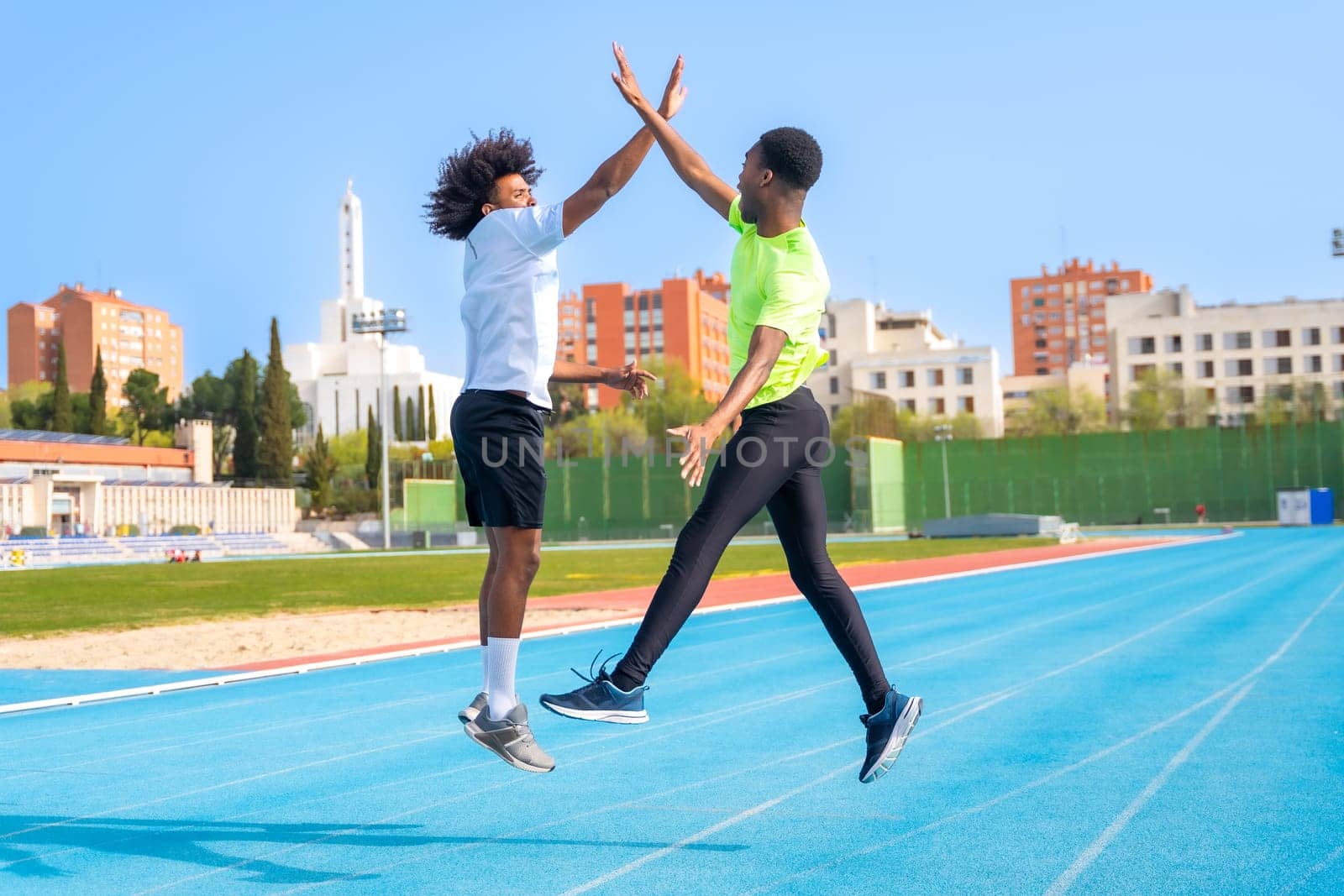 African american young runners jumping high-fiving in a running track by Huizi