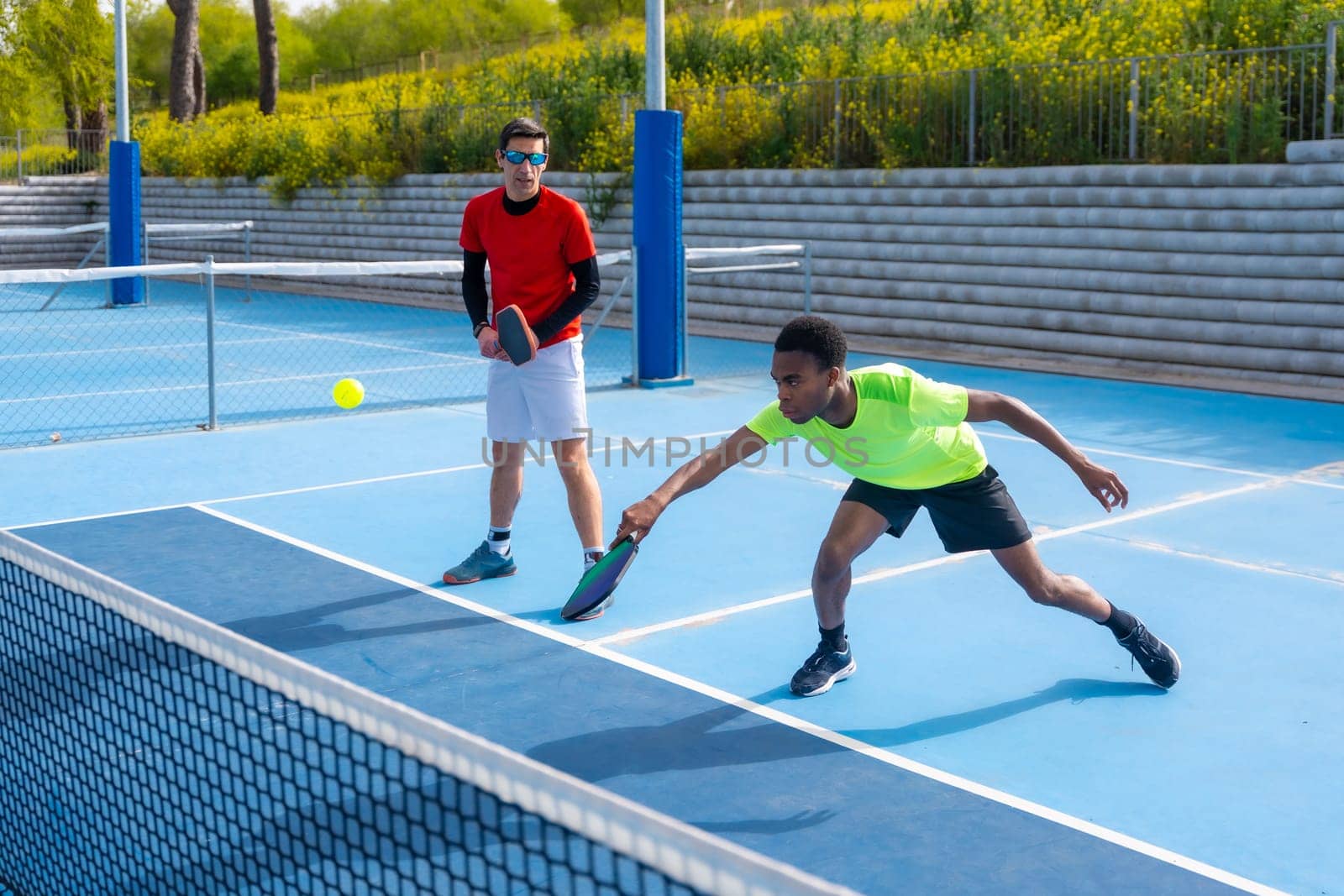 African man trying to reach the ball playing pickleball with a caucasian male partner in an outdoor court