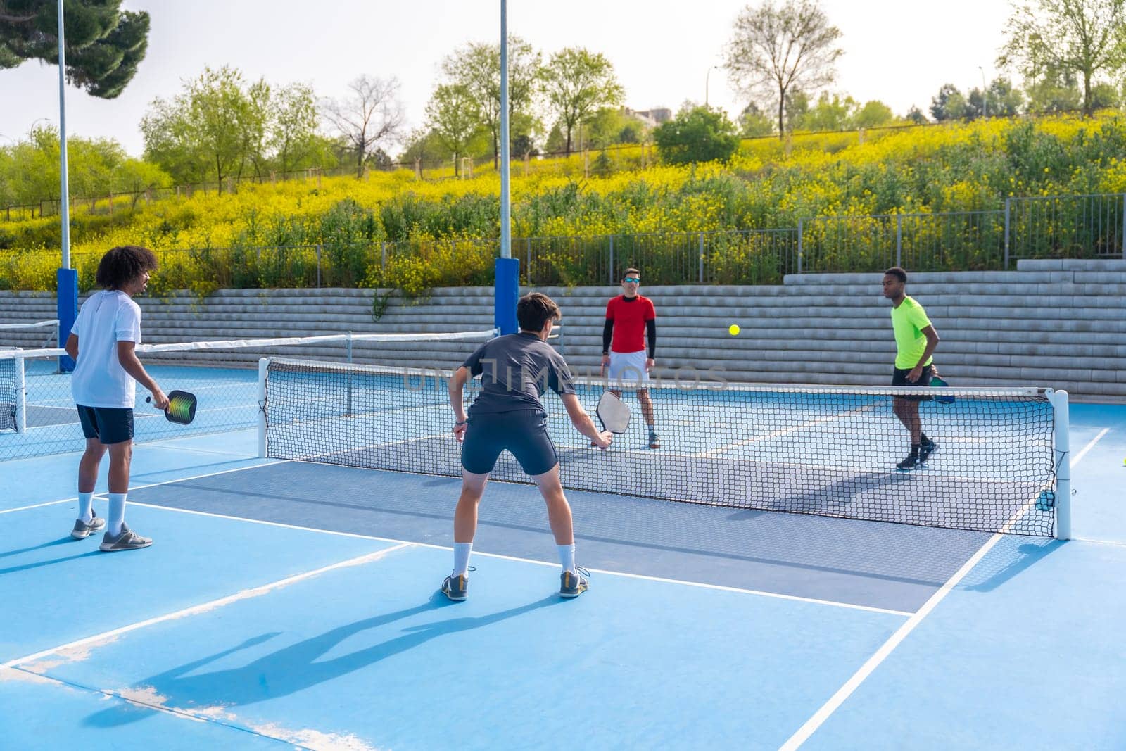 Full length photo of a group of four multi-ethnic friends playing pickleball in an outdoor court
