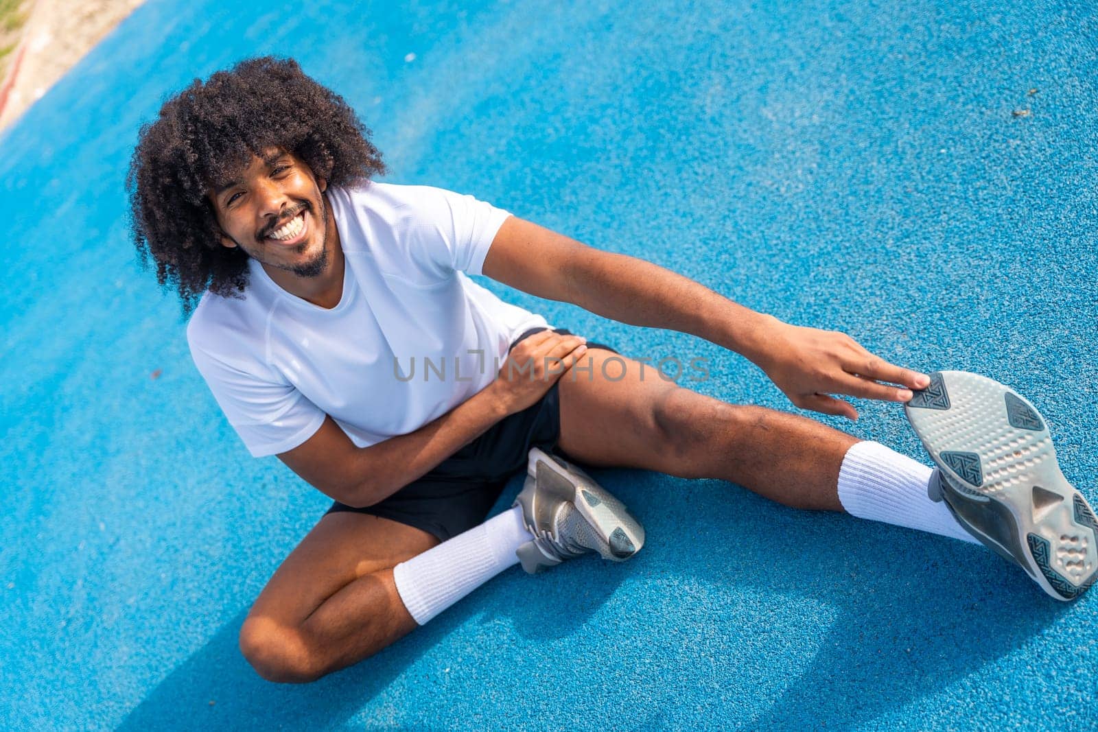 Sportive man with afro hairstyle warming up and stretching by Huizi