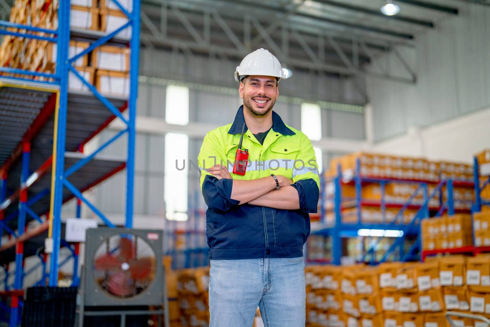 Professional warehouse worker stand with arm-crossed and smiling also look at camera stand in front of shelves with cardbox of product in workplace. by nrradmin